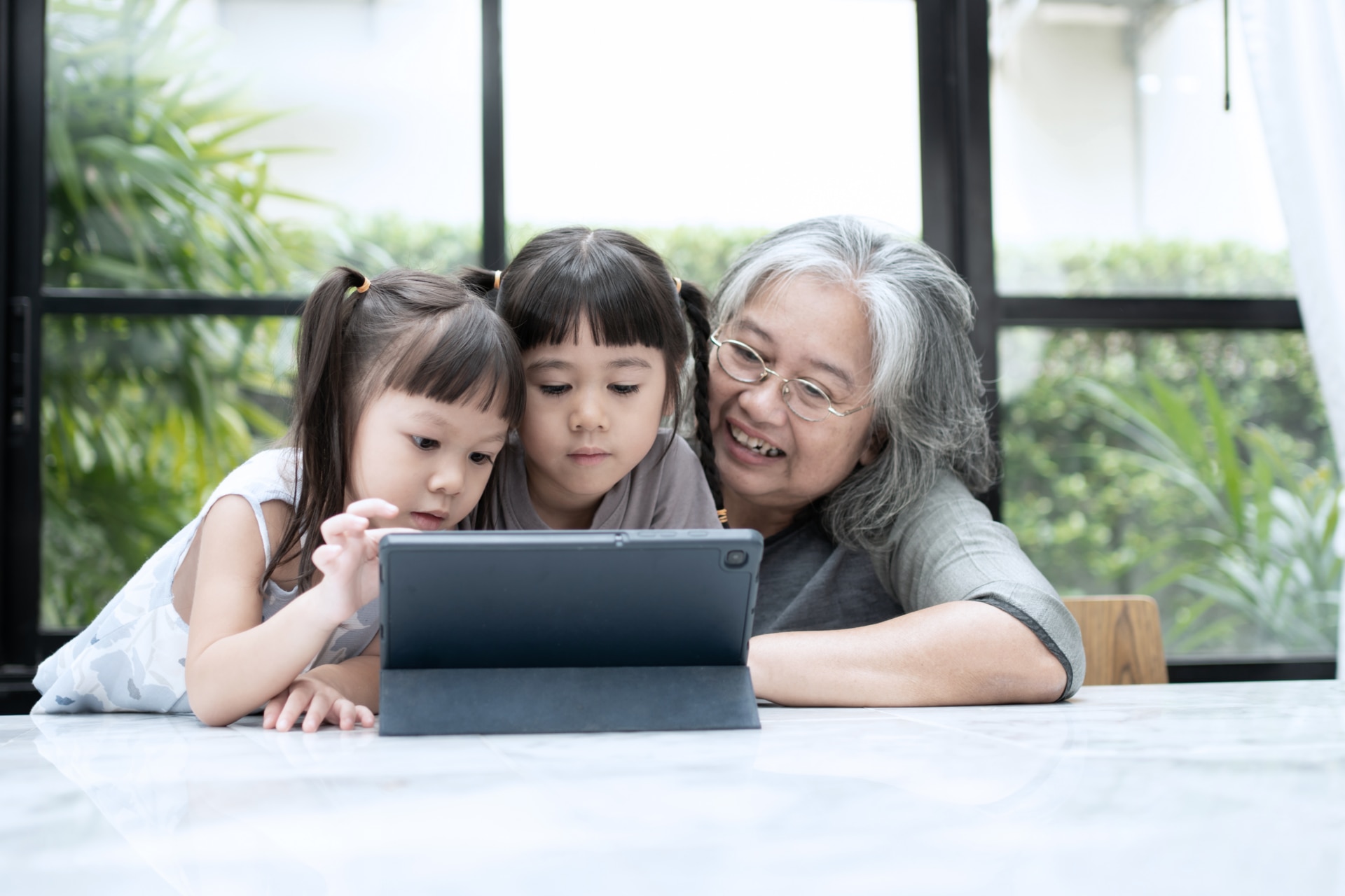 A grandmother watches her two grandchildren use a tablet.