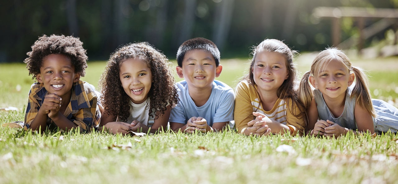 Portrait, diversity and children on grass, friends and summer break with smile, chilling and relax. Face, kids and young group in park, multiracial and fun on vacation, weekend and joyful together; Shutterstock ID 2282044185; purchase_order: Pediatric Conference; job: 600868; client: Katarina Schiffer; other: Phonak