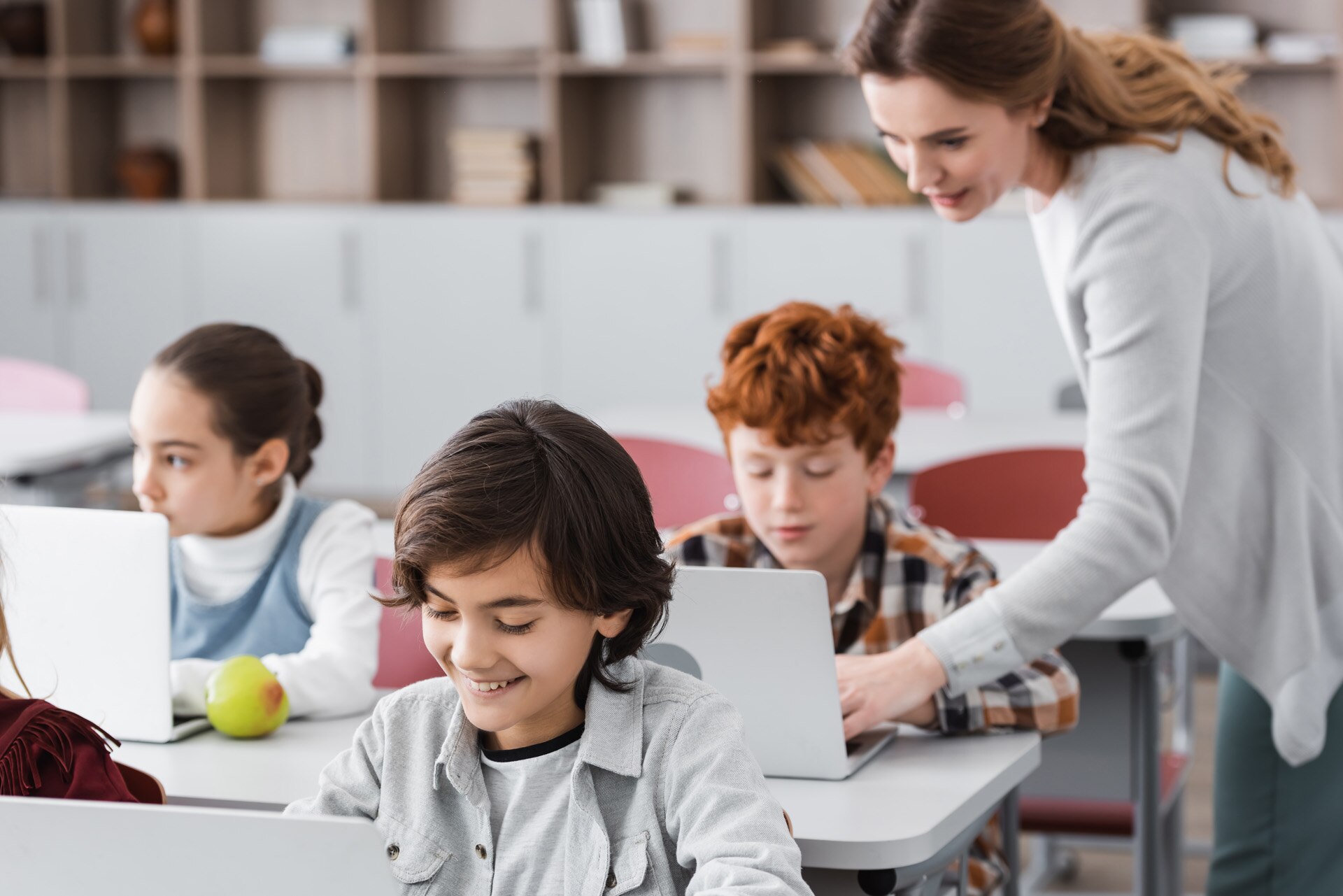 teacher helping schoolboy working on laptop during lesson