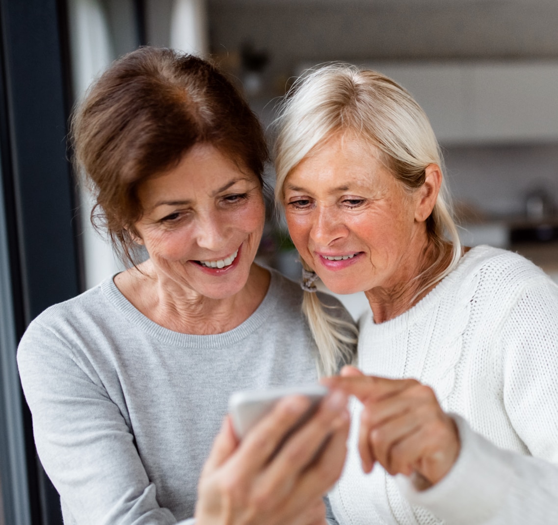 Group of senior friends at home, using smartphones.