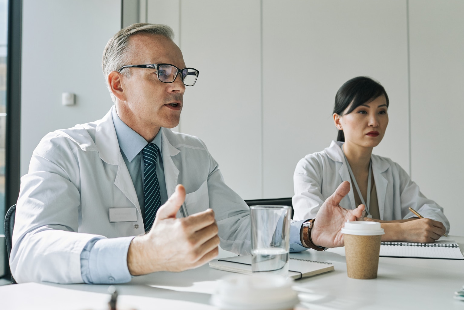 Portrait of mature doctor sitting at meeting table in conference room while speaking during medical seminar