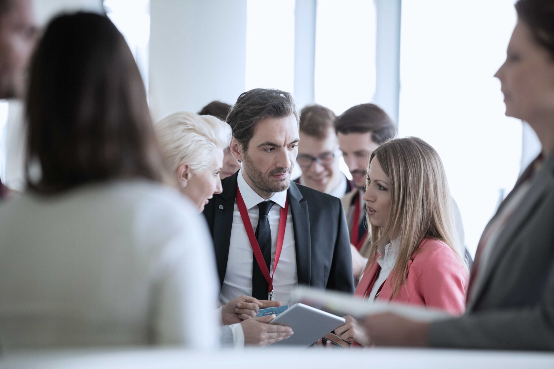 A man standing in a crowded room listening to two women, one on each side of him as they look at a document together.