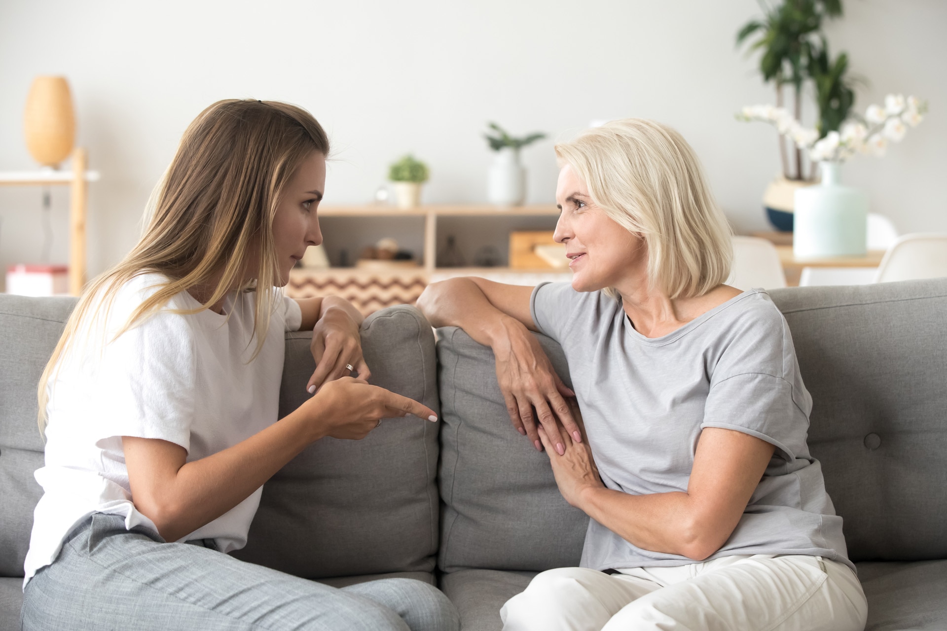 Middle aged woman sitting on sofa in living room with millennial female communicating at home. Mother and daughter spend time together talking having conversation. Warm trustful relationships concept.