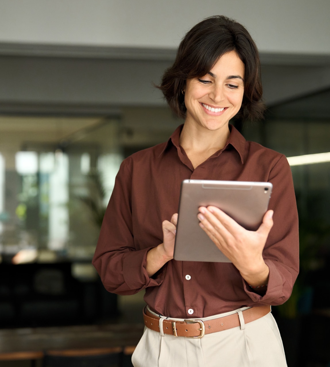 Smiling young adult Hispanic businesswoman leader or entrepreneur, company worker using tablet at work. Happy busy female professional executive holding tab computer standing in office.; Shutterstock ID 2510015493; purchase_order: 103318; job: Project Number ; client: Michael Blackburn ; other: Phonak 