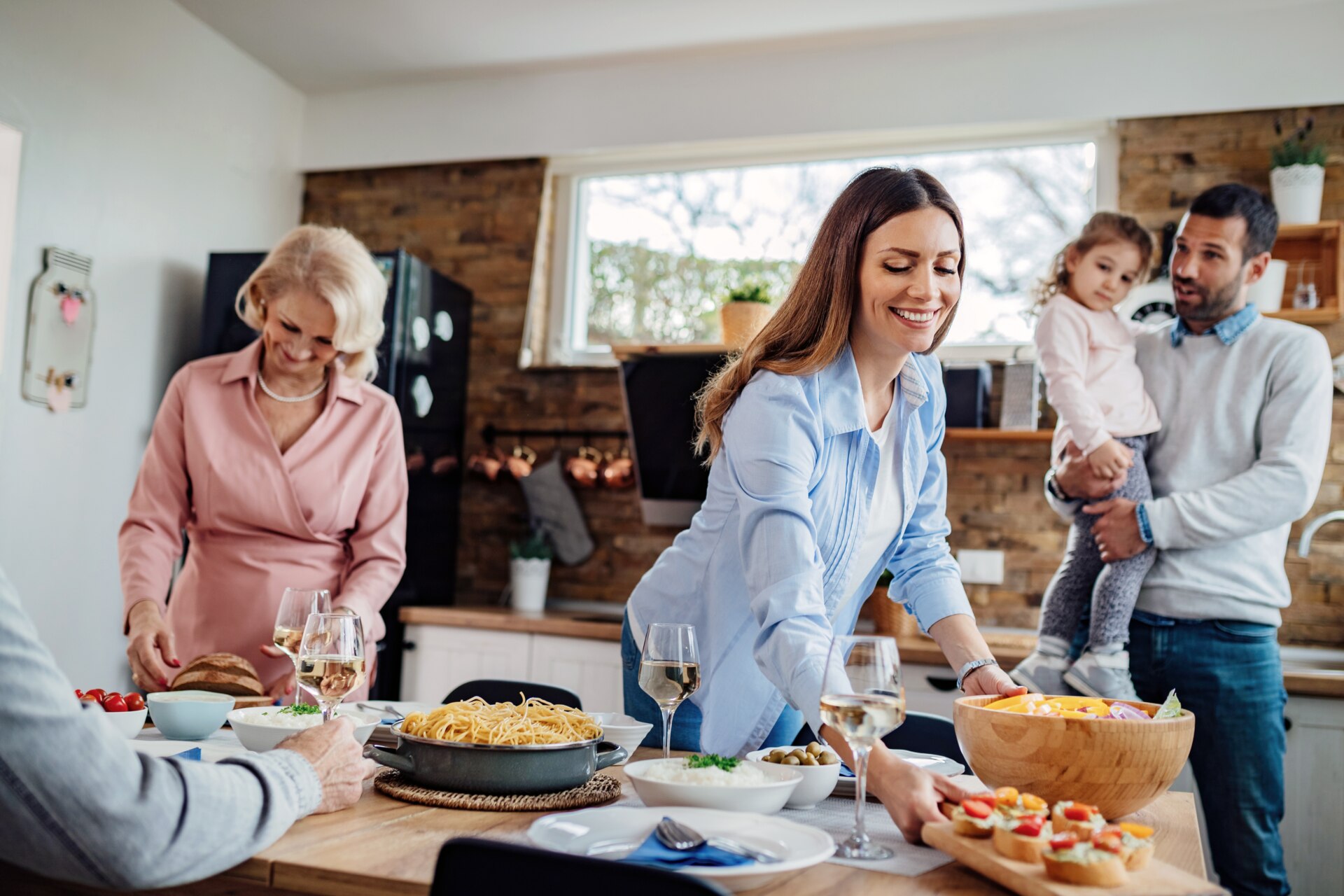 Young happy woman setting dining table for multigenerational family lunch at home. 