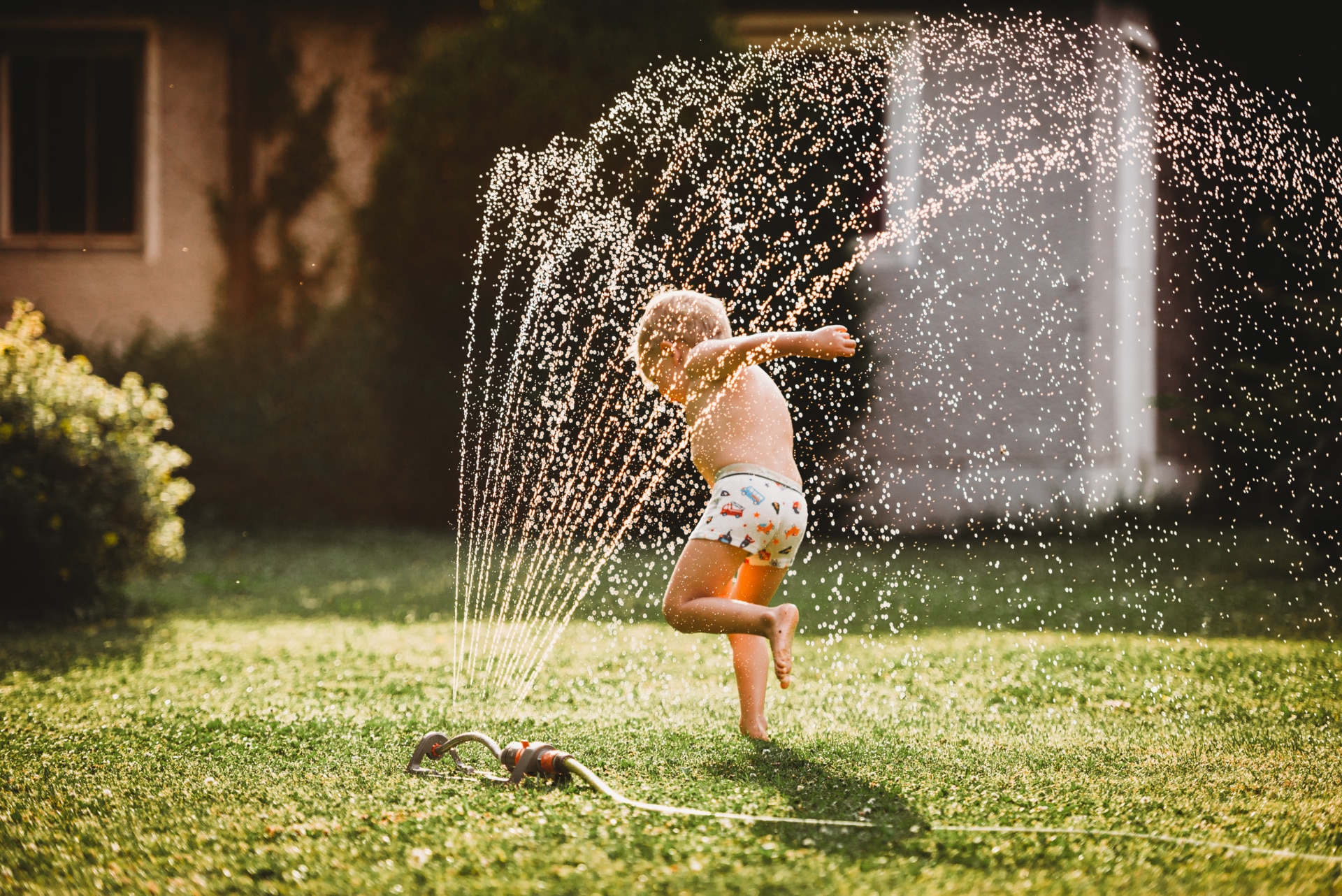 Ragazzo che corre sotto l'acqua di un irrigatore in un giardino.