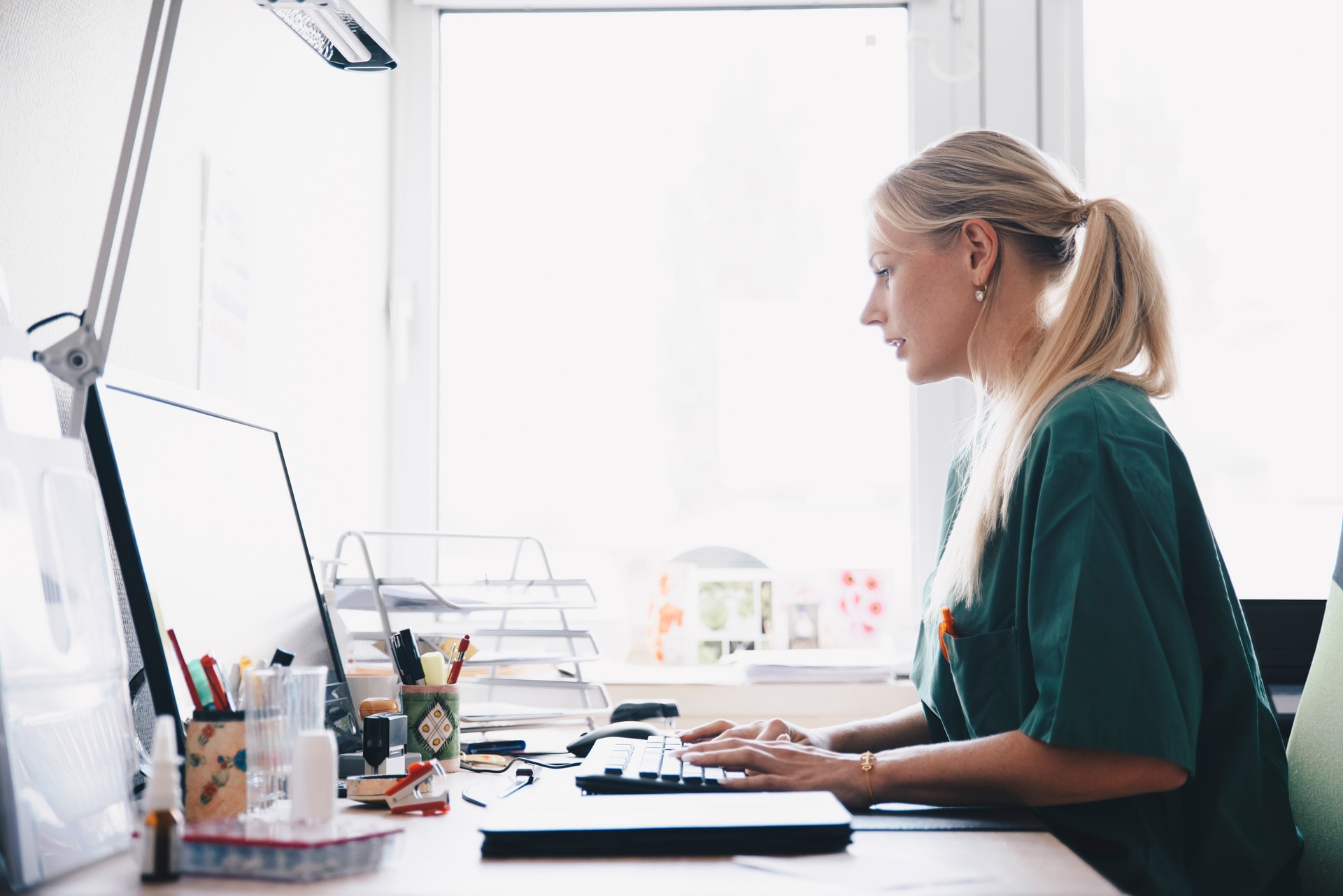 Female doctor filling patient data in front of a desktop.