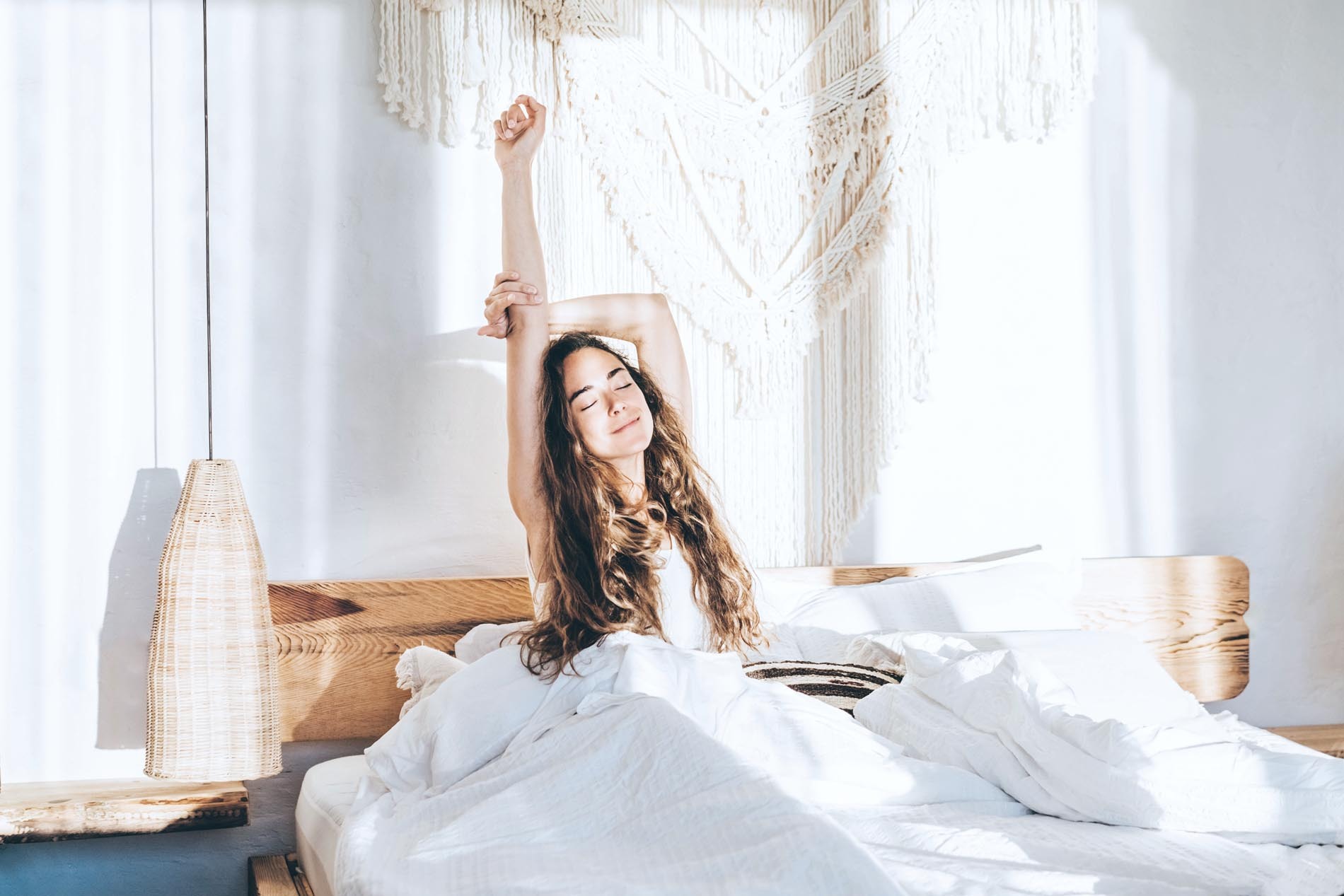 Mujer relajándose en una cama. Mujer estirando los brazos en la cama