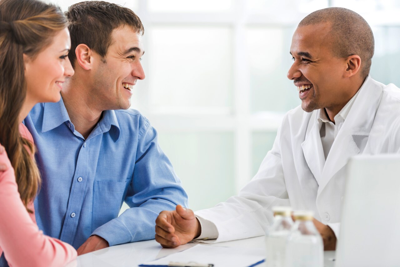 Alegre médico comunicándose con una joven pareja en su consulta.