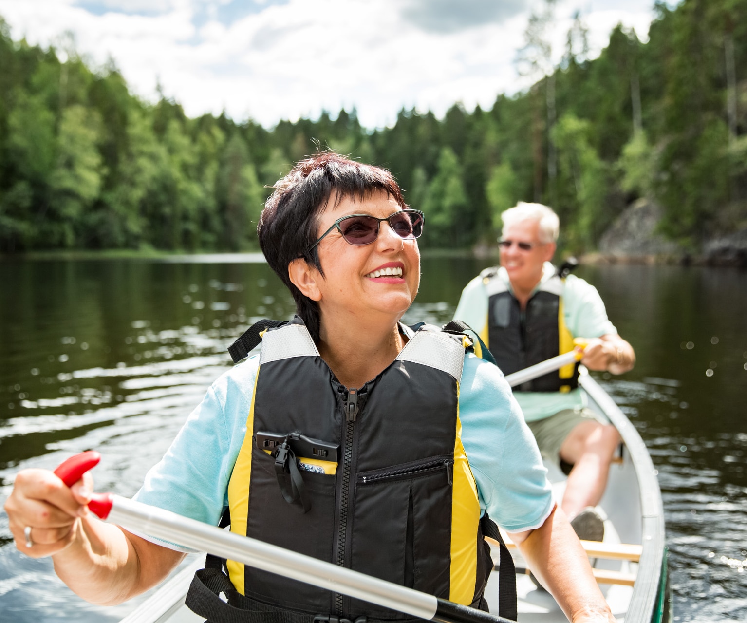 Pareja madura feliz con chalecos salvavidas haciendo piragüismo en un lago forestal. Día soleado de verano. Turistas viajando por Finlandia, viviendo aventuras.