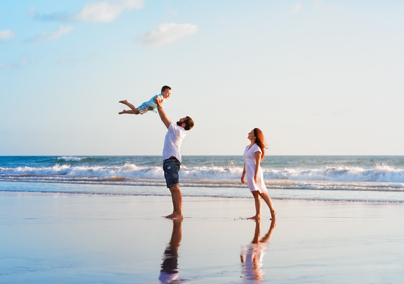 Happy family holidays. Joyful father, mother, baby son walk with fun along edge of sunset sea surf on black sand beach. Active parents and people outdoor activity on summer vacations with children.; Shutterstock ID 717546631; purchase_order: -; job: -; client: -; other: -