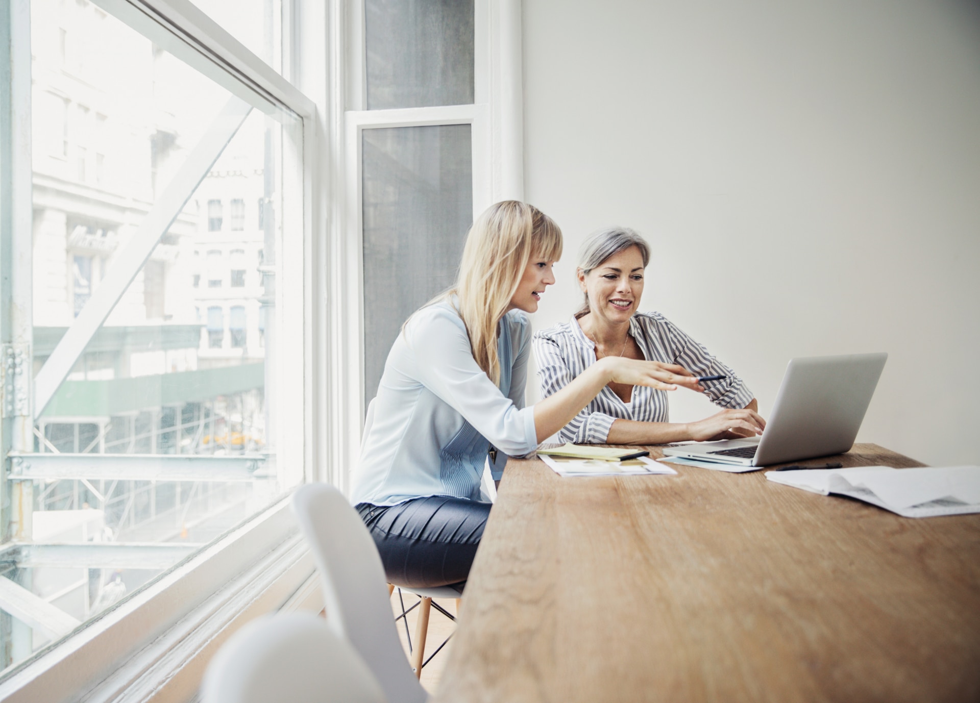 Two female coworkers discussing something while working on a laptop.
