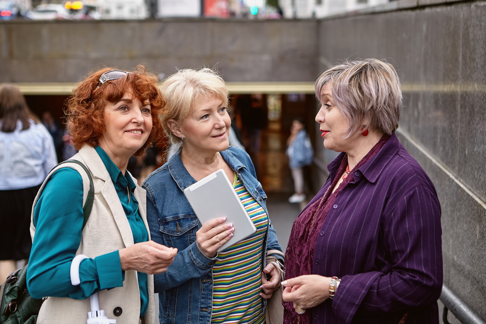 Three senior European women talk on the street near the descent to the underpass.