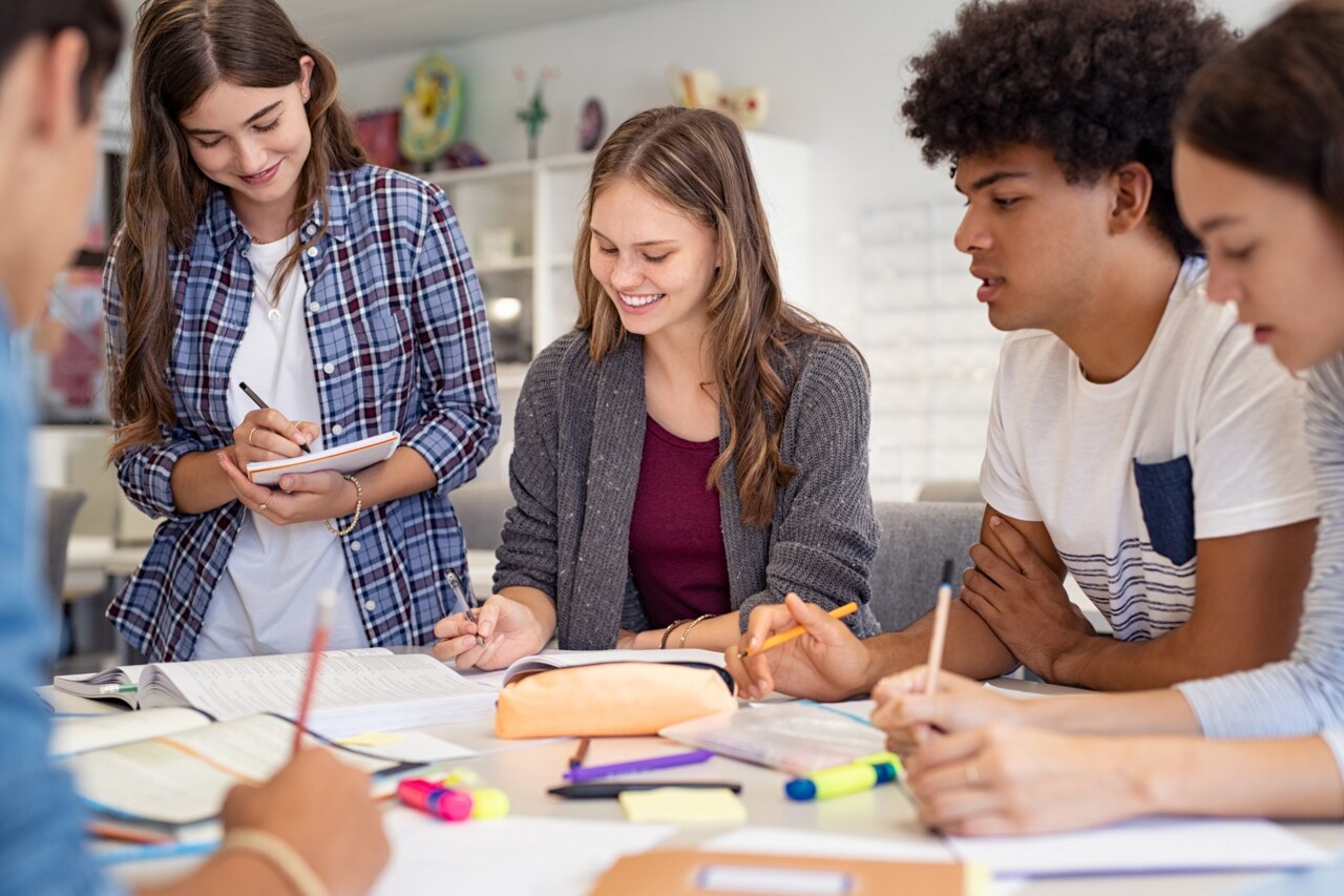 Happy team of high school girls and guys studying together. Group of multiethnic classmates smiling in university library. Group of young people sitting at table working on school assignment.