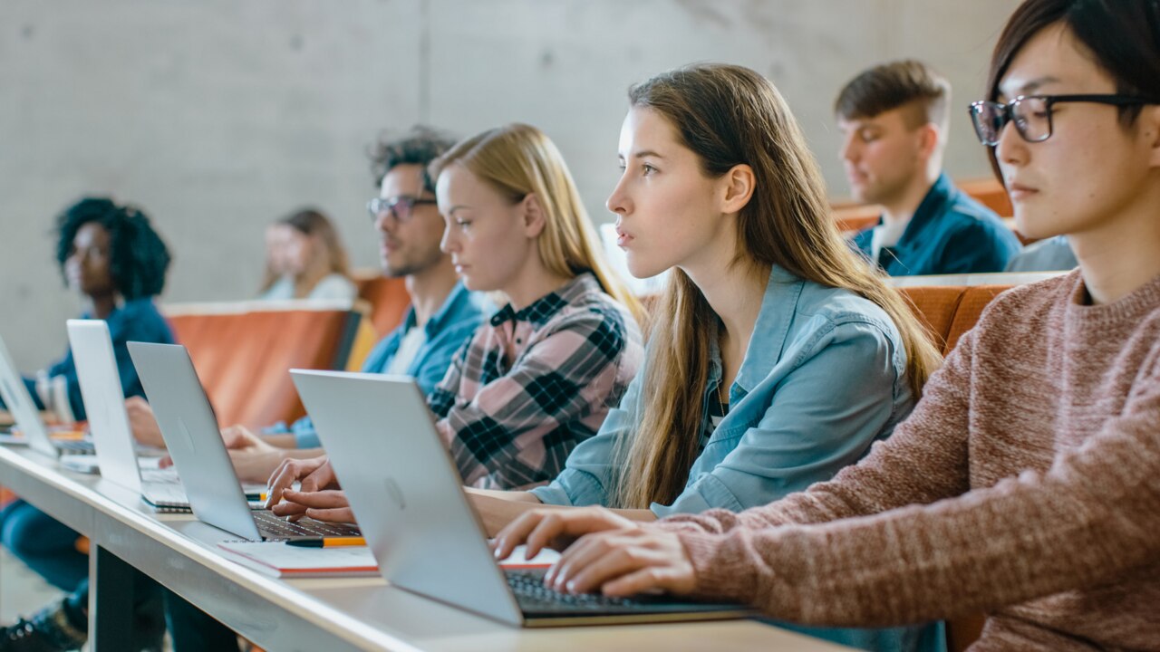 Large Group of Multi Ethnic Students Working on the Laptops while Listening to a Lecture in the Modern Classroom. Bright Young People Study at University.