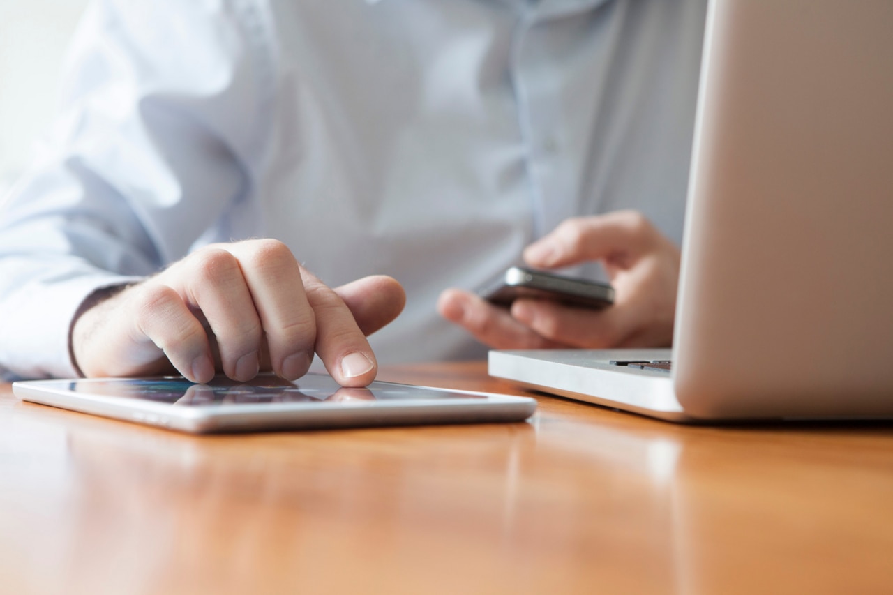 Man is typing on tablet while holding a smartphone in his left hand.