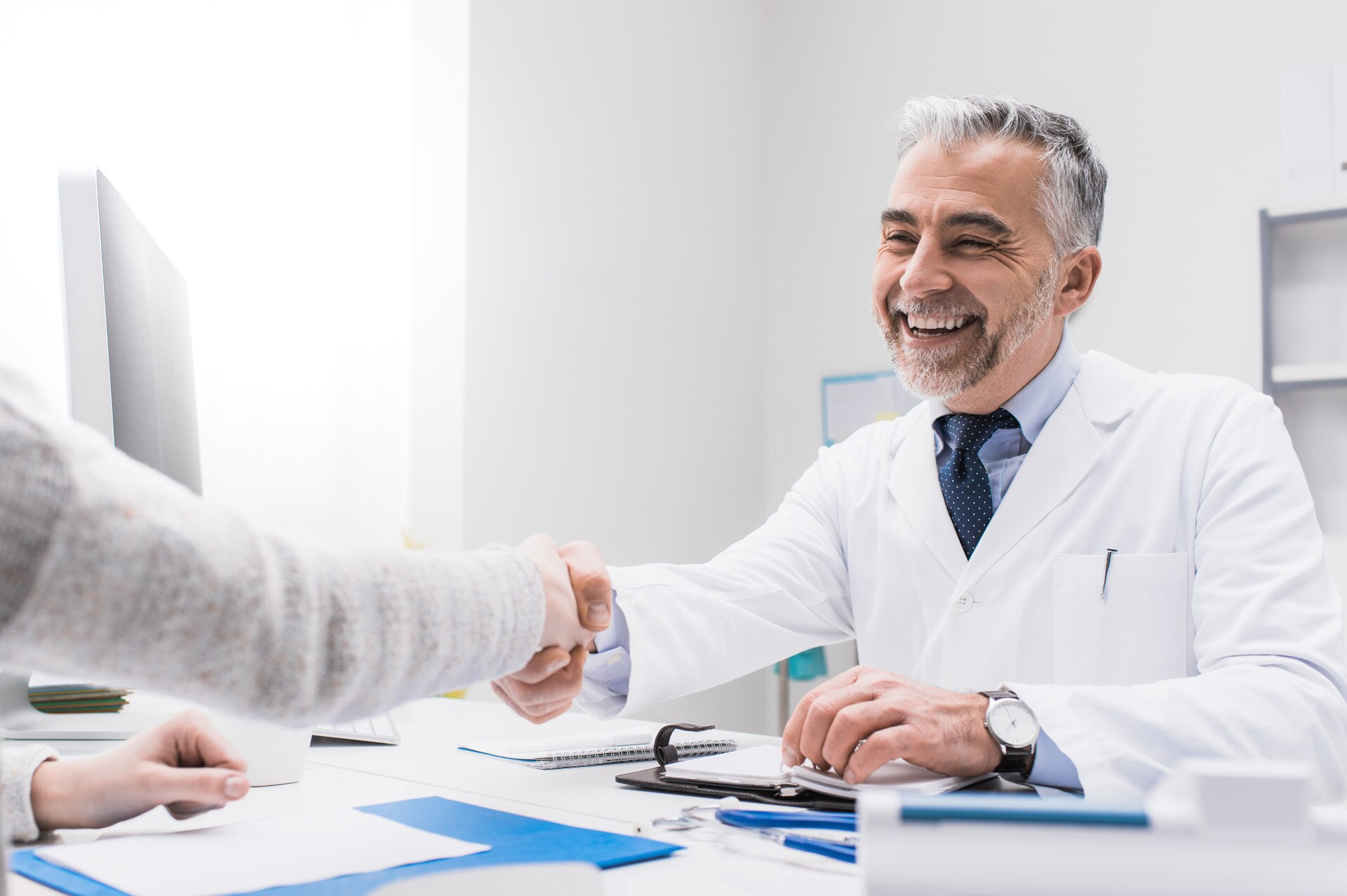 Smiling doctor and female patient shaking hands, healthcare professionals concept