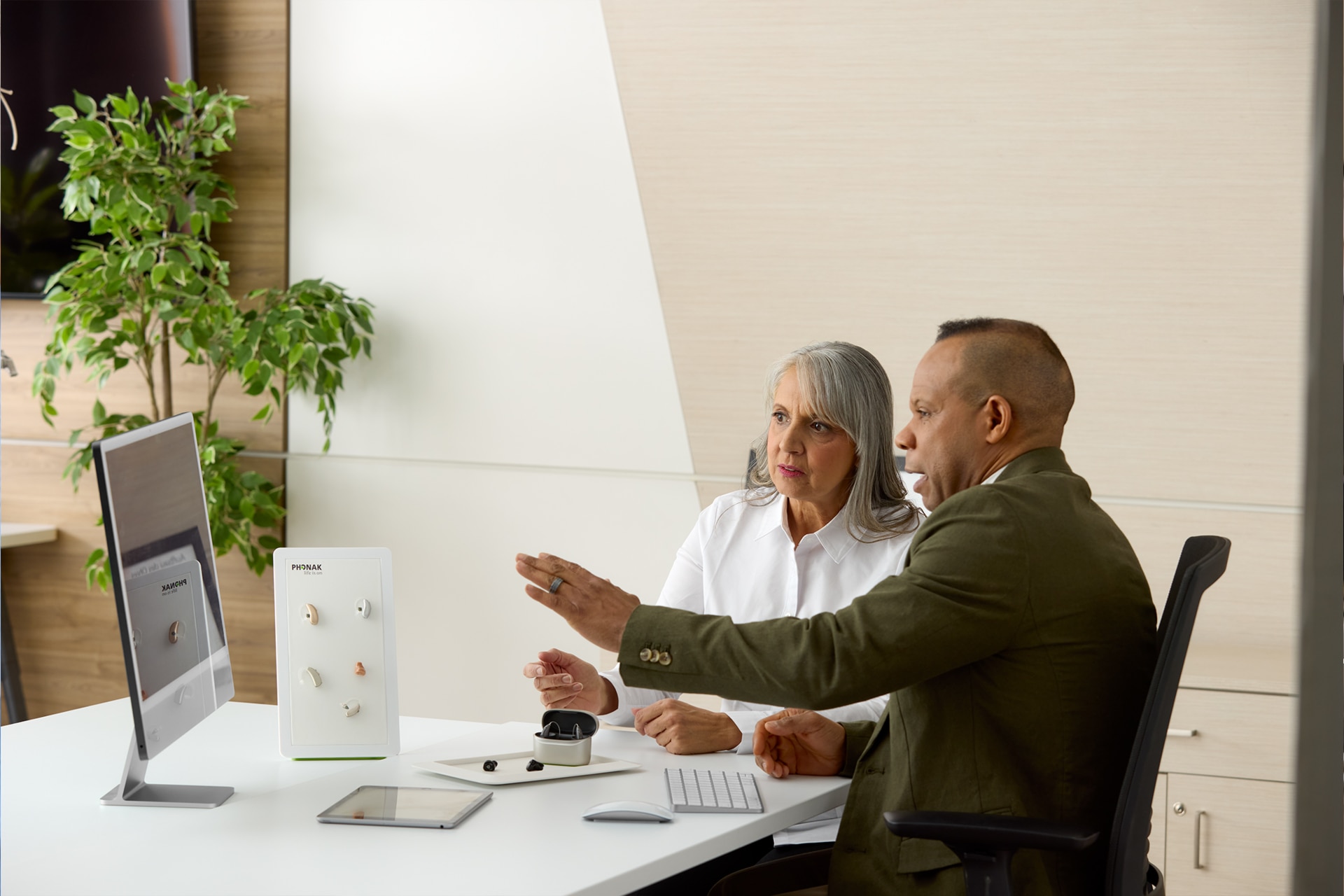Audiologist showing hearing aid options at a clinic desk