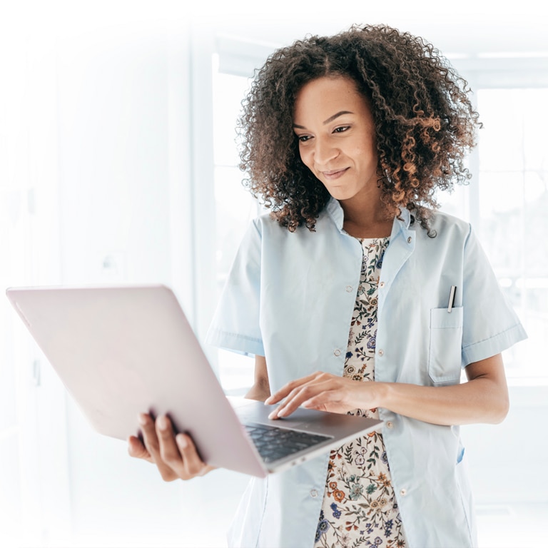 Woman standing indoors with her laptop in hand.