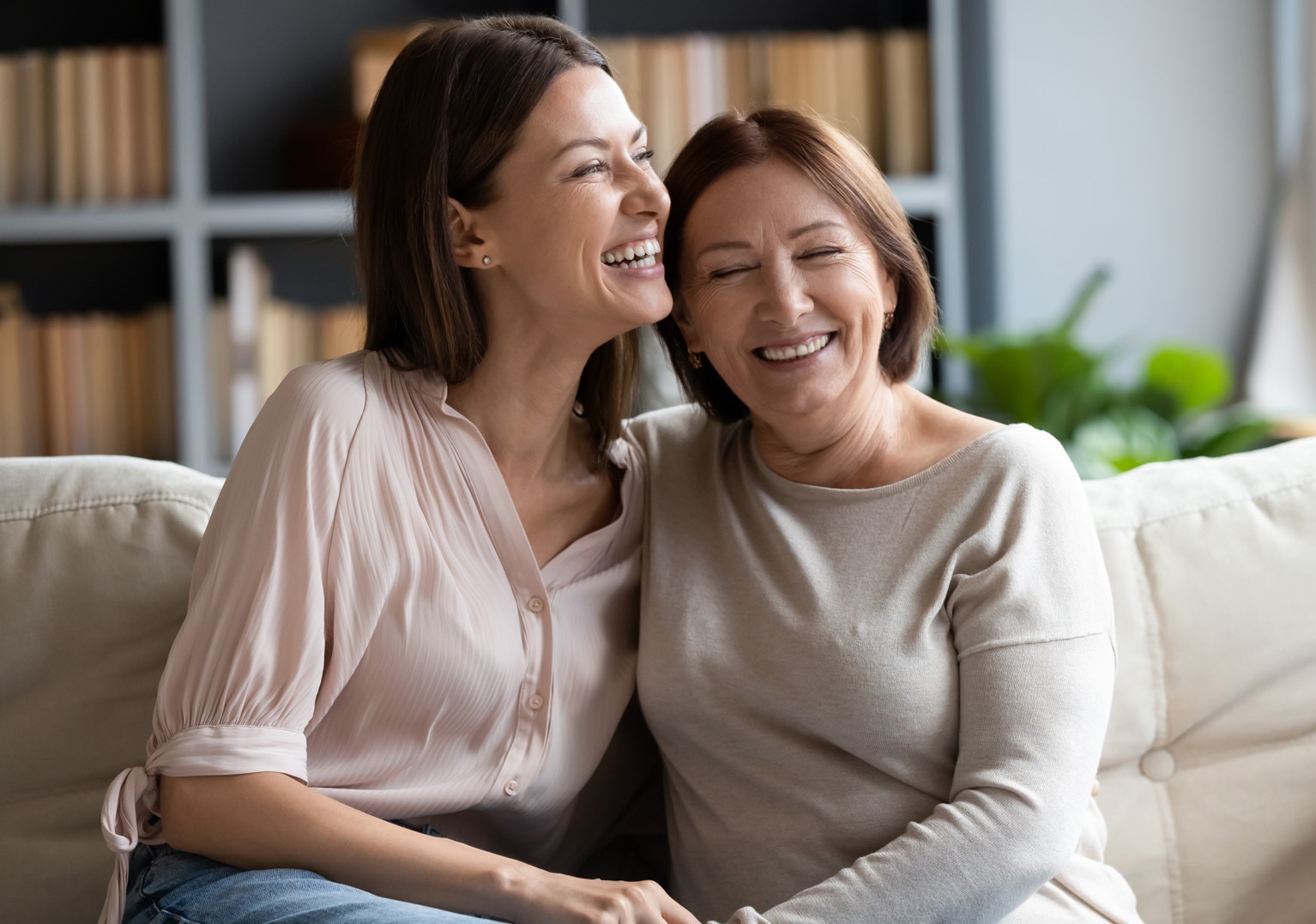 A mother with her grown-up daughter sitting on a couch, laughing together A mother with her grown-up daughter sitting on a couch, laughing together