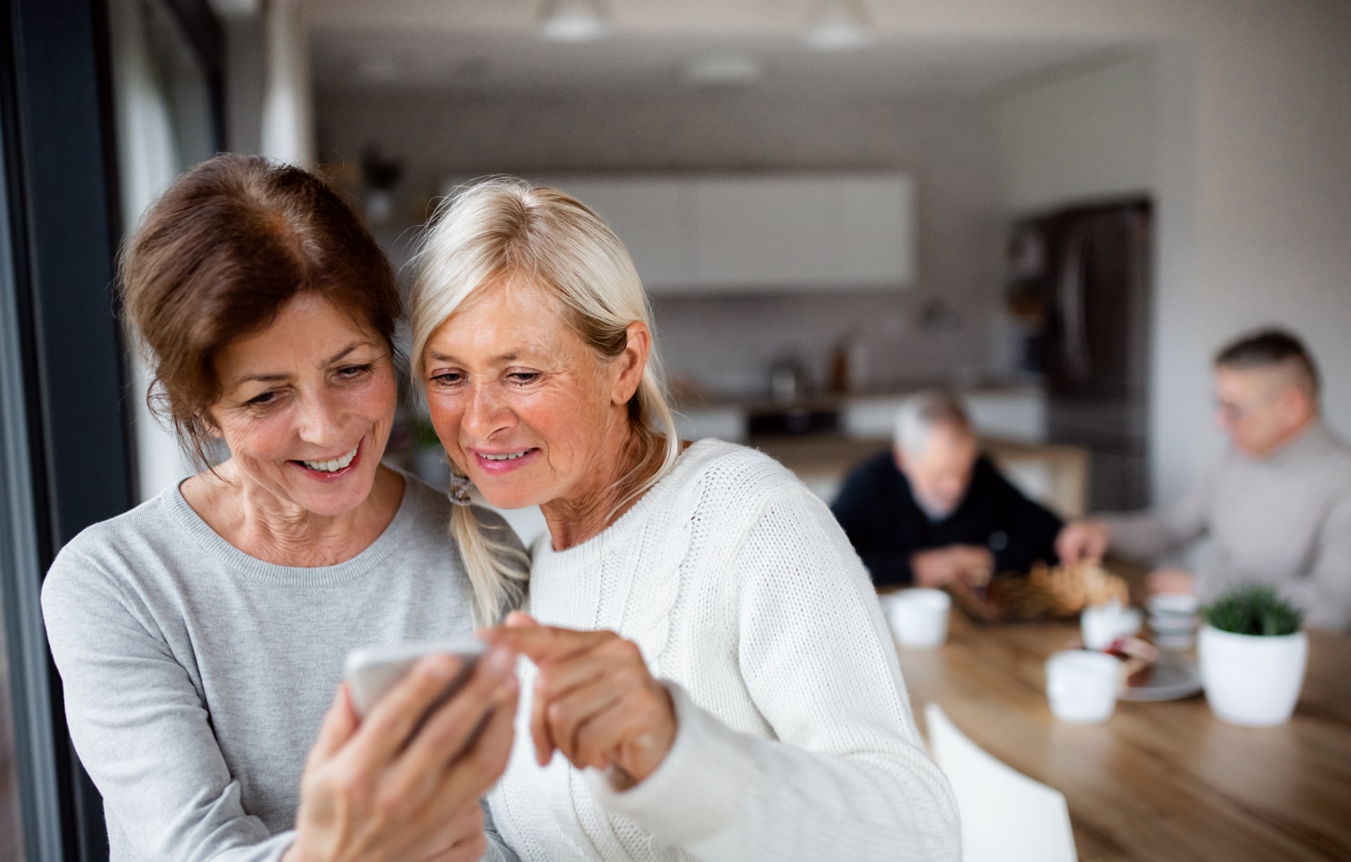 Group of senior friends at home, using smartphones.