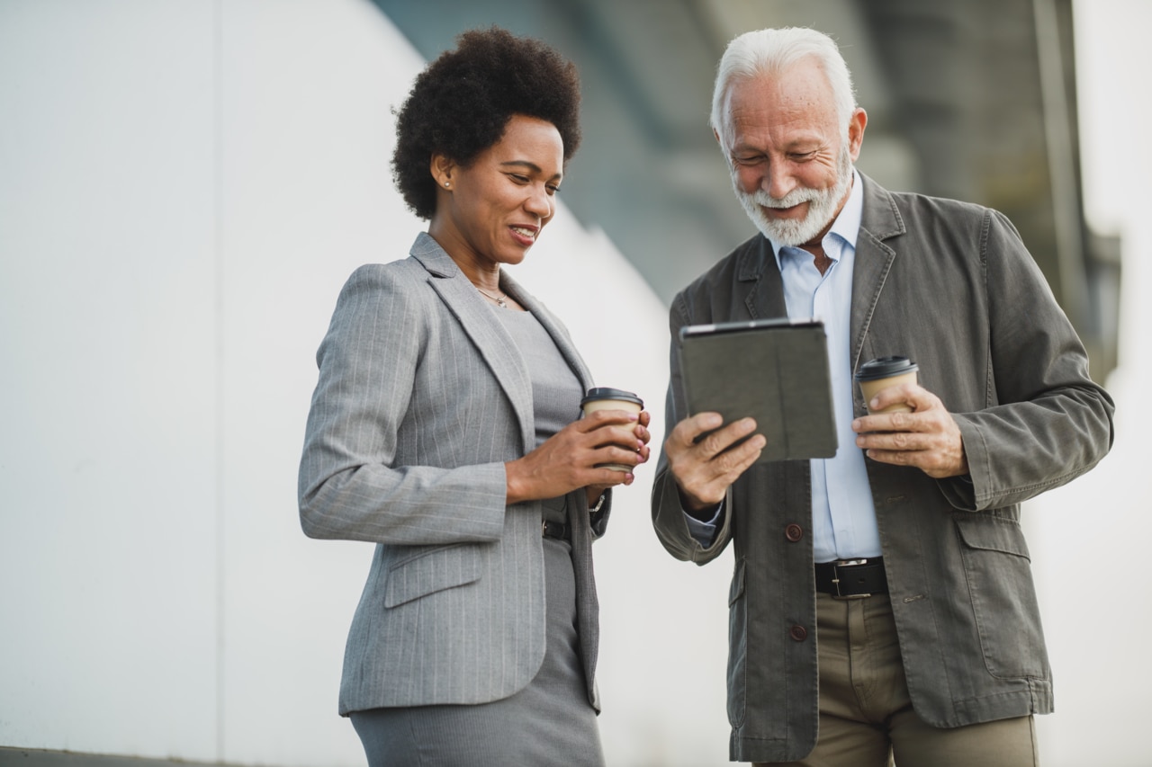 Shot of two successful multi-ethnic business people talking and using digital tablet while having a coffee break outdoors.