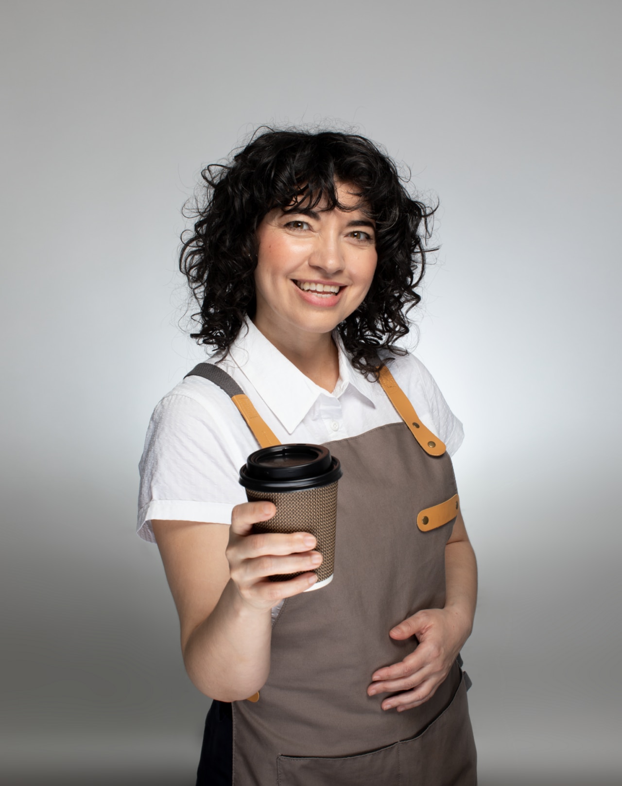 Leende kvinnlig barista står med en stor kopp kaffe i handen.