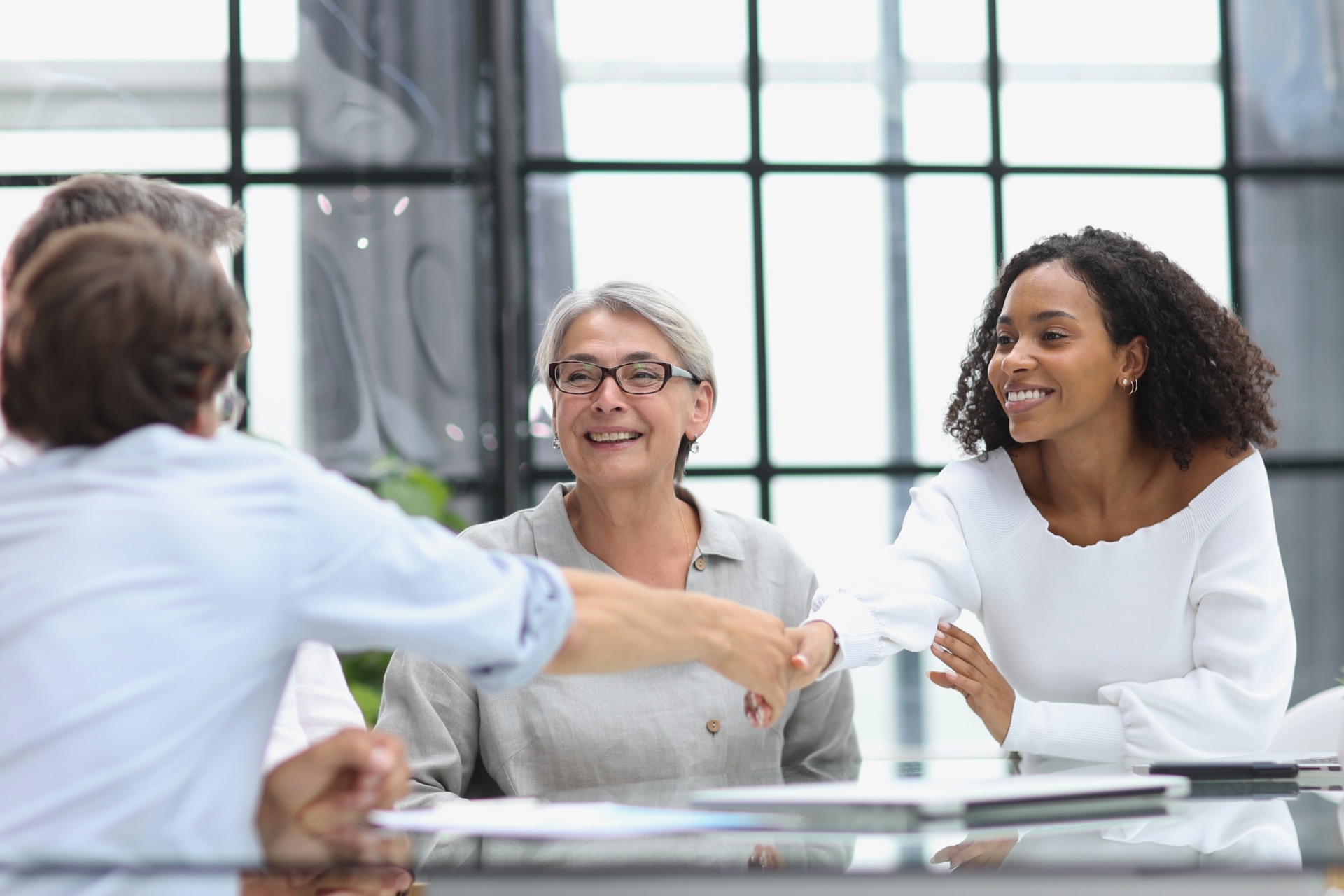 A woman in an office shaking hands with a man at a table in a modern office A trio working together on something