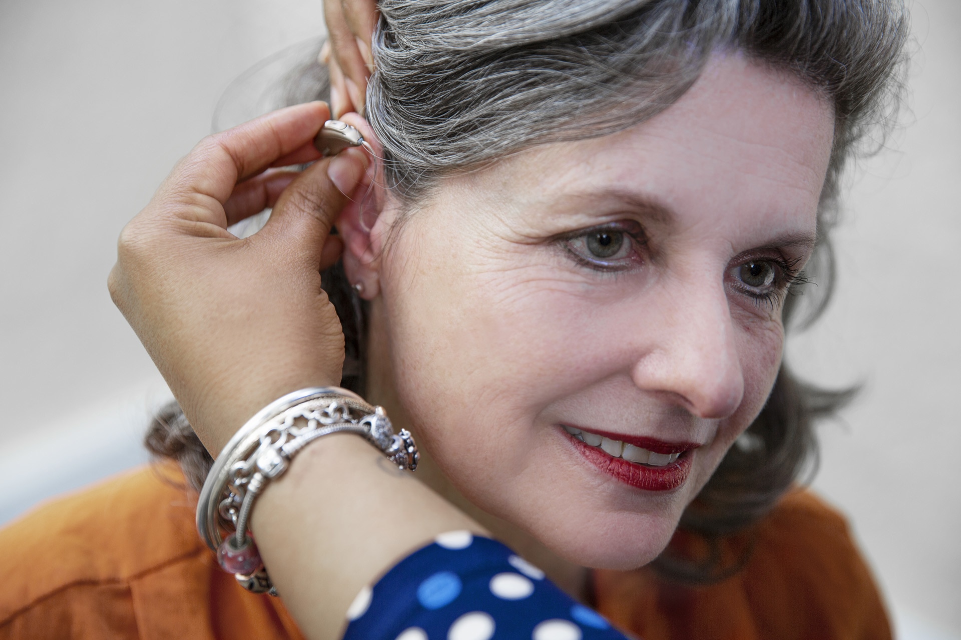 Middle aged woman inserting hearing aid in her right ear.