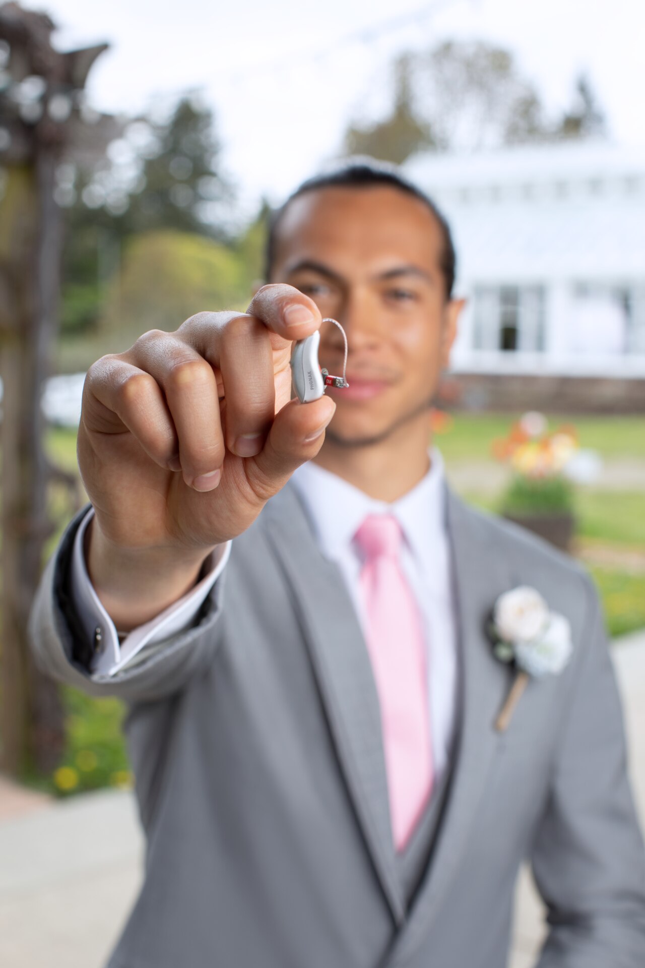 Phonak Audéo L-R hearing aid in a hand of a young male in a wedding suit.