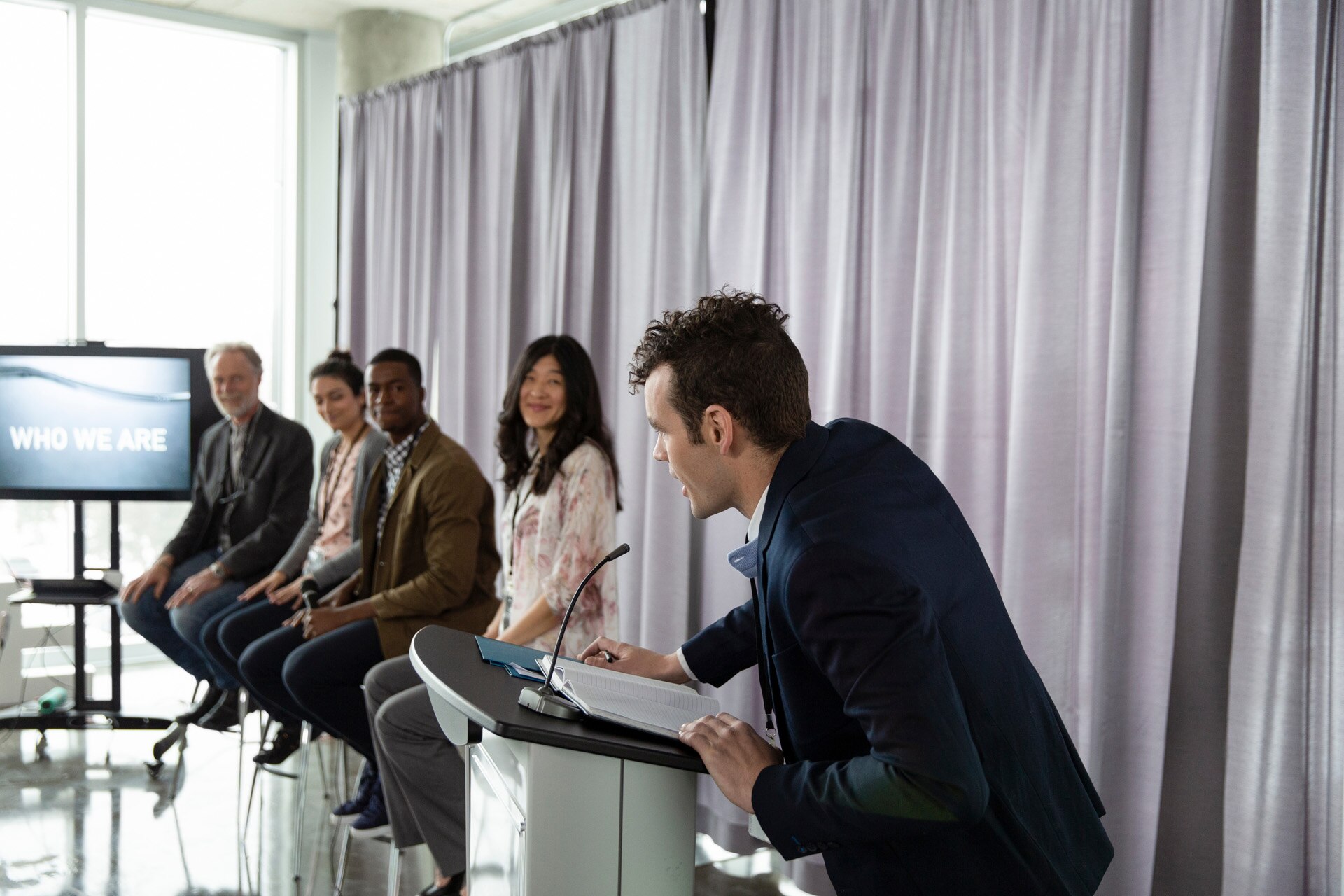 Man at podium introducing panel of motivation speakers at conference