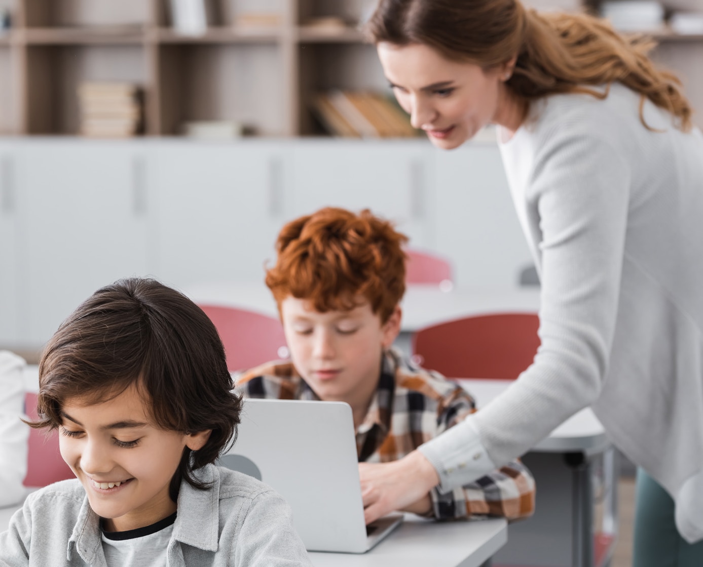 teacher helping schoolboy working on laptop during lesson