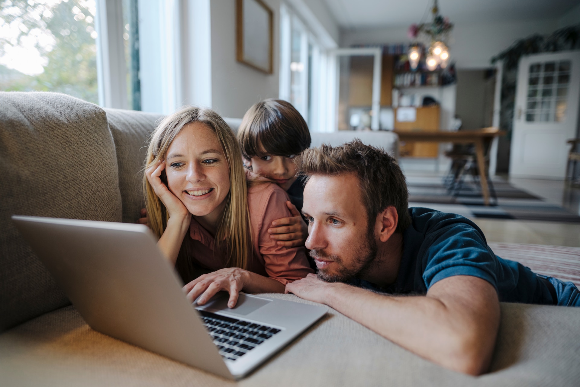 Happy family on couch watching something on a laptop. Happy family lying on couch- using laptop