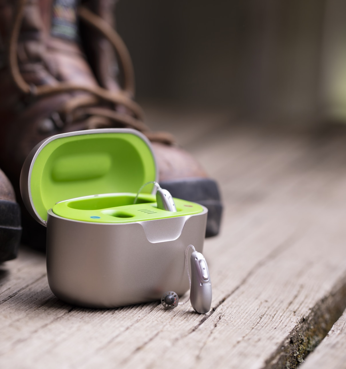 Hearing aid portable charger next to Audeo Lumity hearing aid and a hiking boot. lorem ipsum