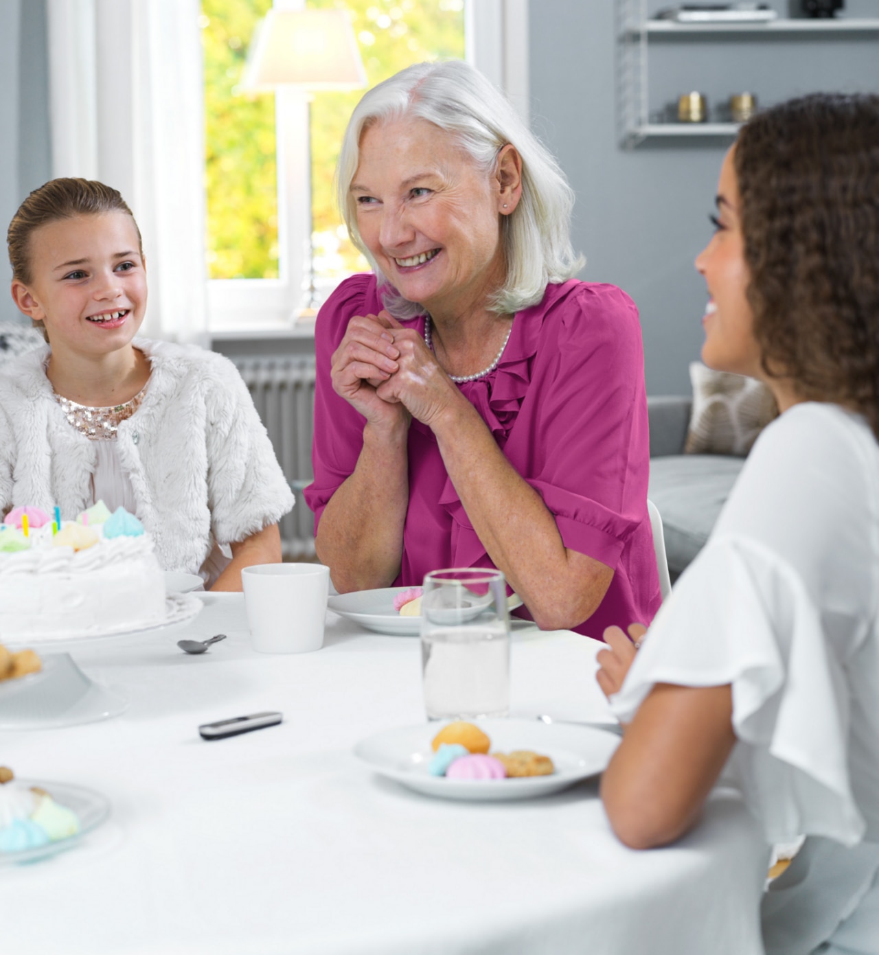 Grandmother with her two granddaughters sitting at a table - Phonak Roger on microphone in front of them placed on a table. Grandmother with her two granddaughters sitting at a table - Phonak Roger on microphone in front of them placed on a table.