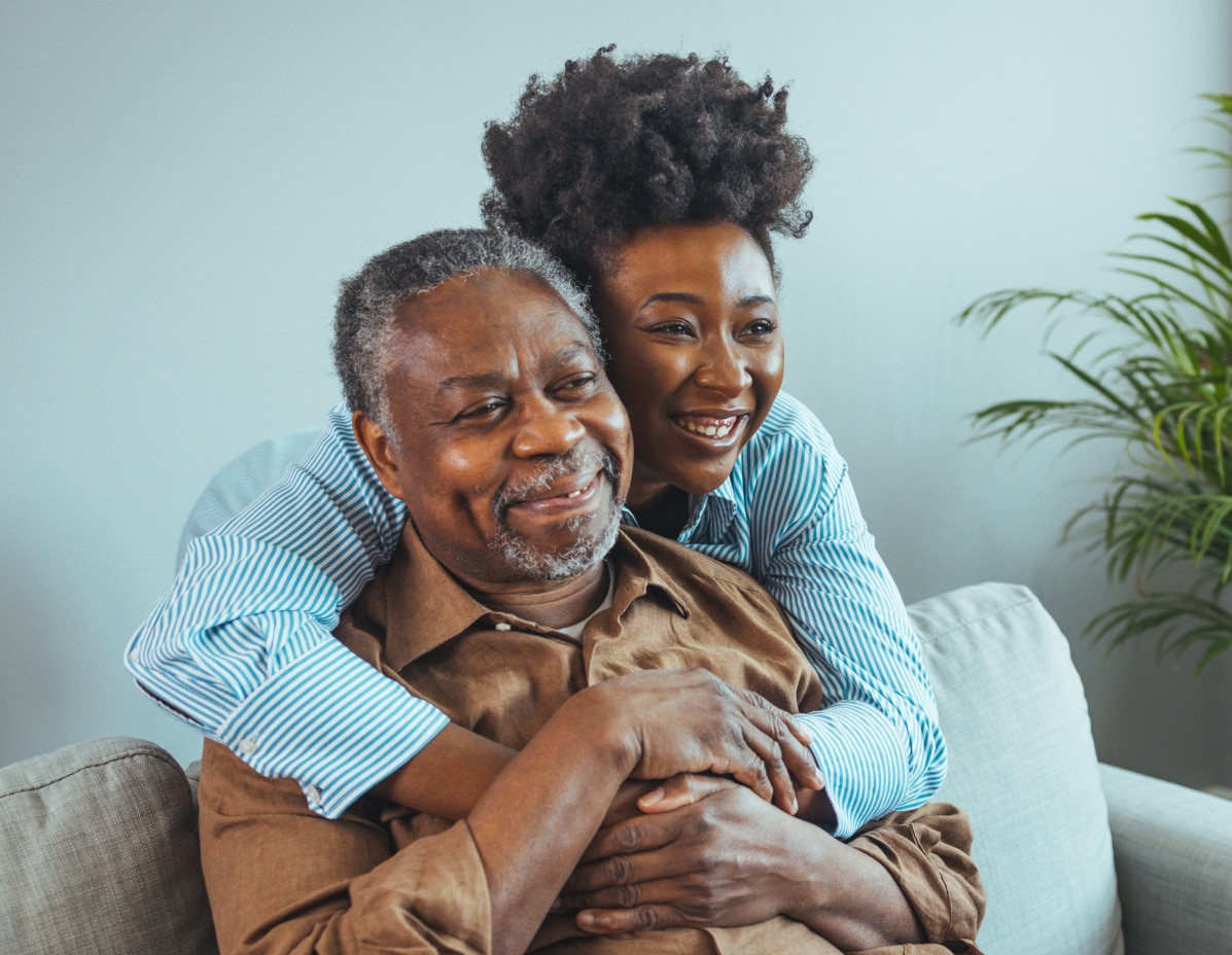 Adult daughter visits senior father in assisted living home. Portrait of a daughter holding her elderly father, sitting on a bed by a window in her father's room Adult daughter visits senior father in assisted living home. Portrait of a daughter holding her elderly father, sitting on a bed by a window in her father's room