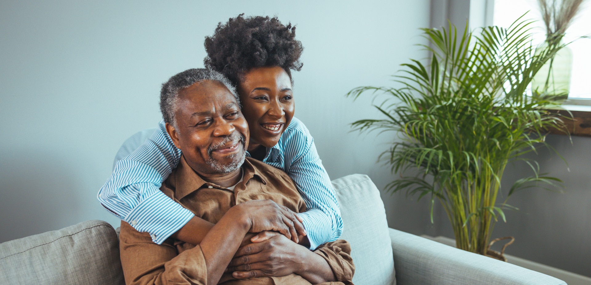 Adult daughter visits senior father in assisted living home. Portrait of a daughter holding her elderly father, sitting on a bed by a window in her father's room Adult daughter visits senior father in assisted living home. Portrait of a daughter holding her elderly father, sitting on a bed by a window in her father's room