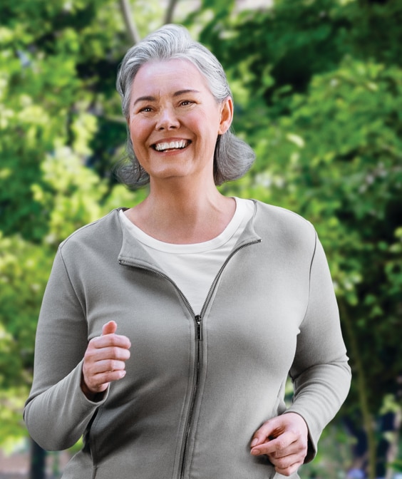 Elderly smiling woman in a grey dress running in the park.