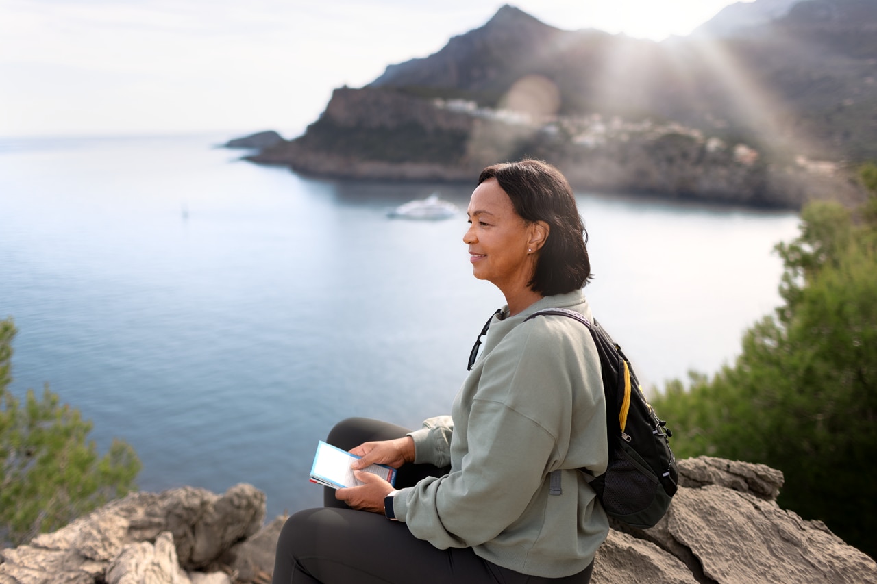 AudeoI Trekking Woman tourist sitting on big stone in the mountains looking at the sea.