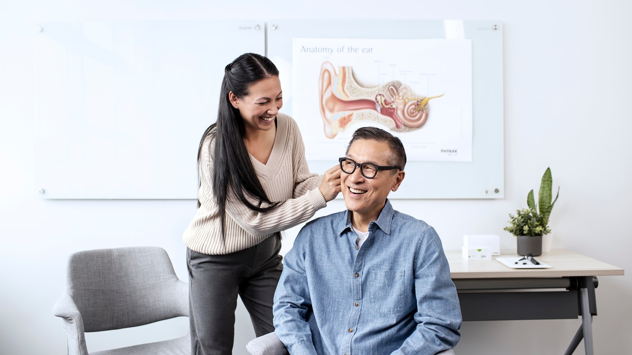 An audiologist adjusts a man’s hearing aids during a clinic visit.