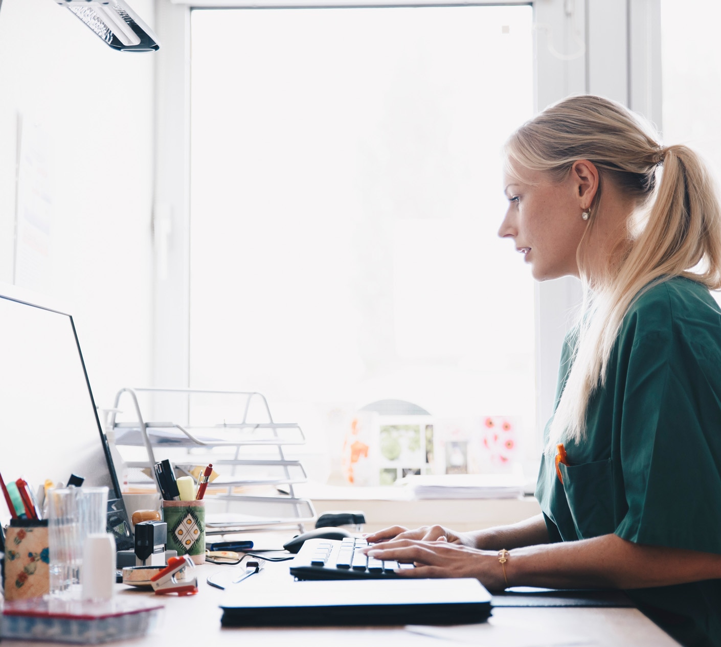 Side view of female nurse working at computer desk against window in office