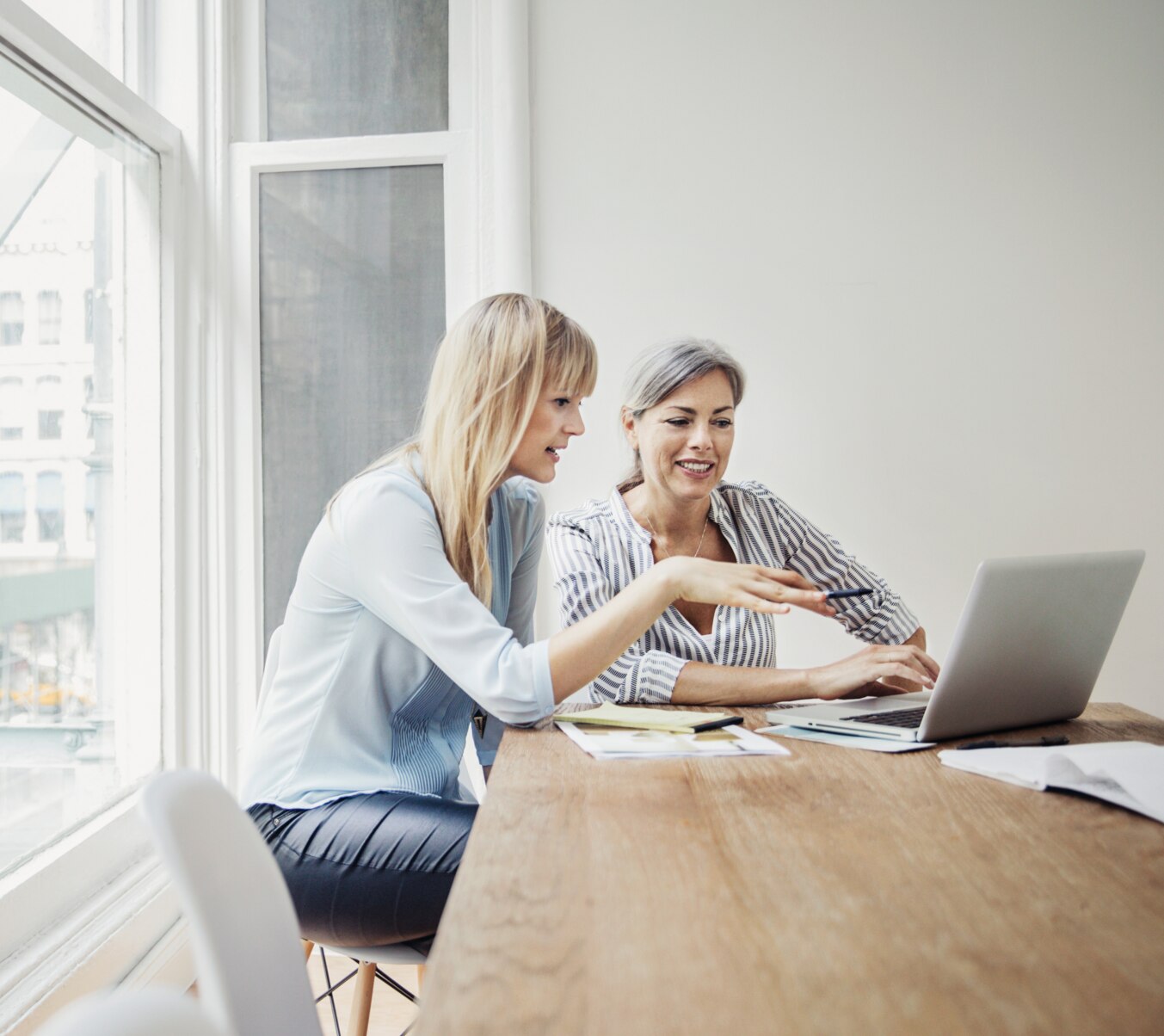 Two female coworkers discussing something while working on a laptop.