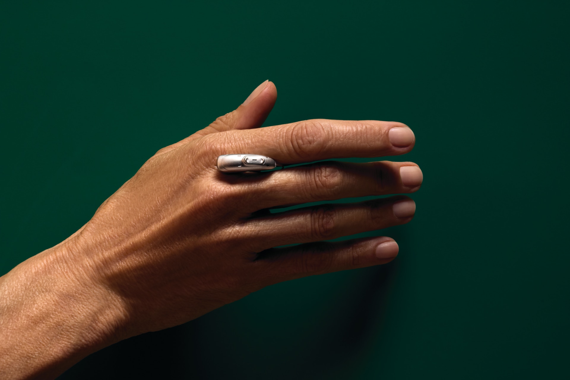 Close-up of a hand resting on a green surface, with Phonak EON hearing aid