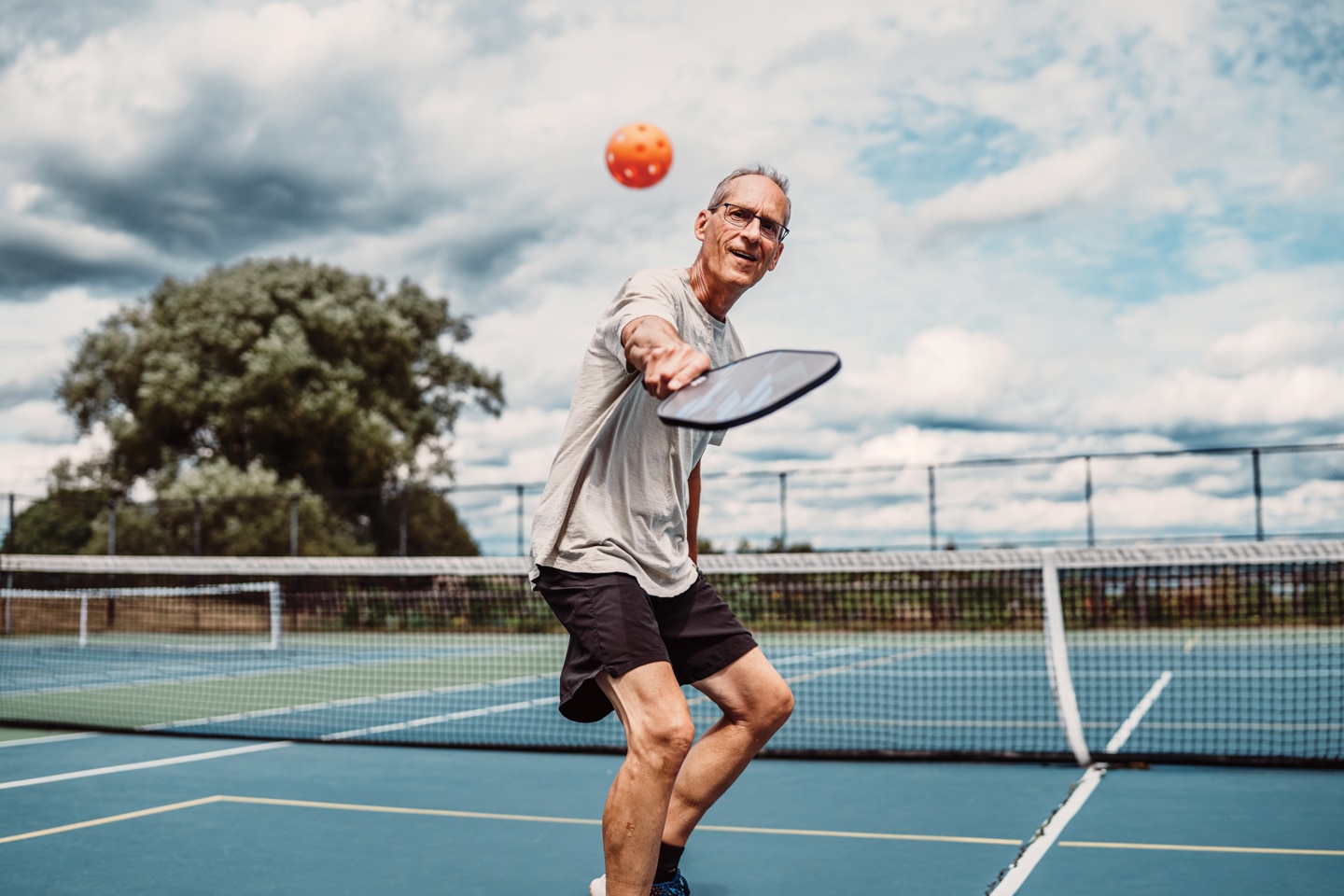 Man wearing gray shirt playing pickleball with orange ball