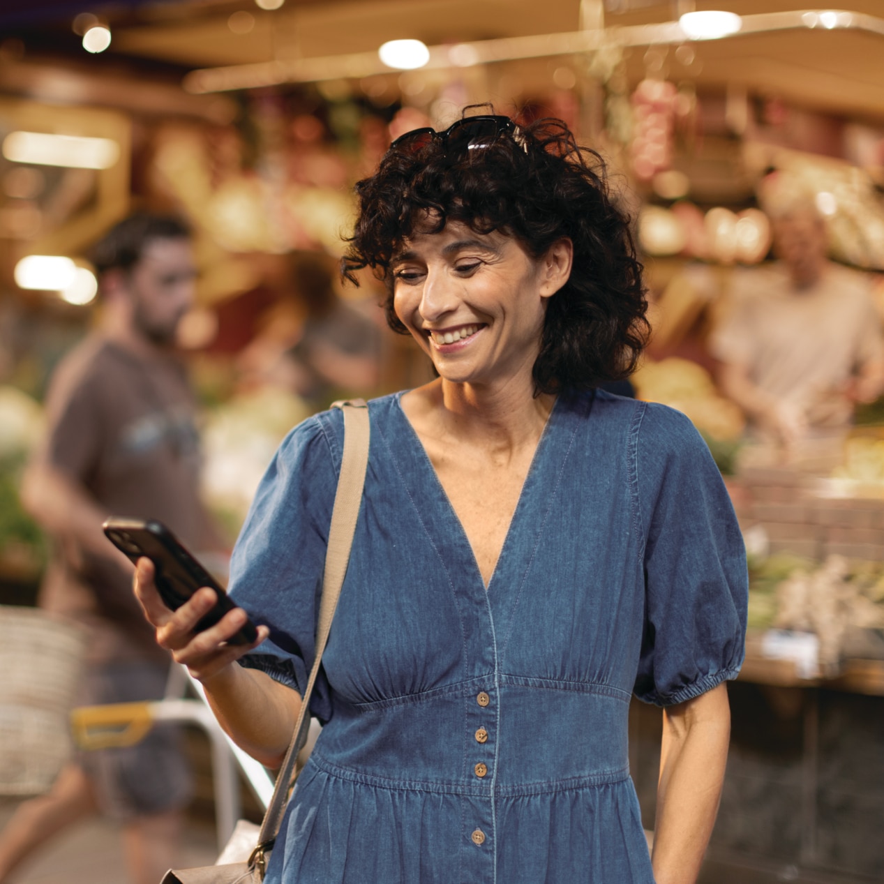A middle-aged woman looking at her phone during shopping, smiling Woman in Market with Phonak Audéo I-R