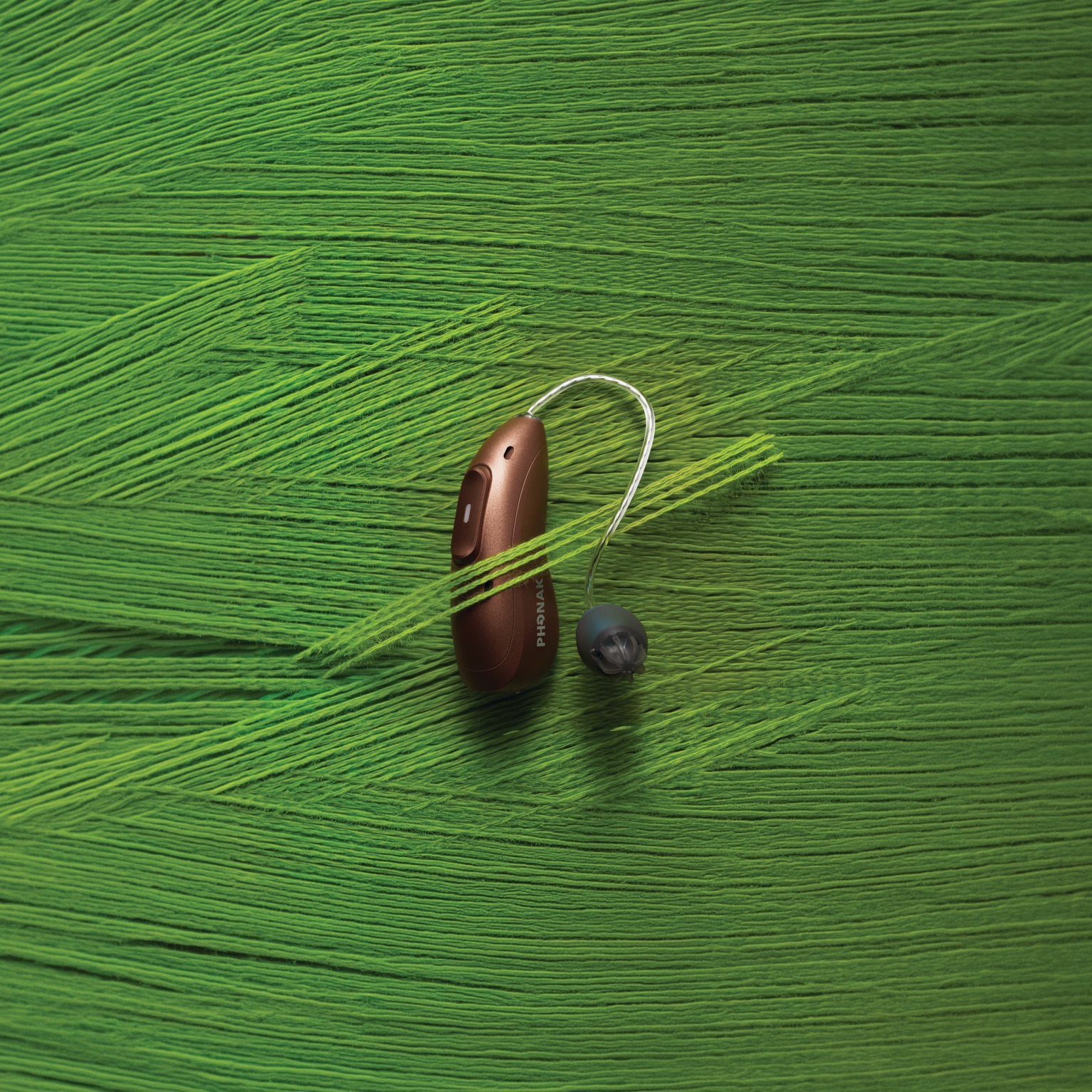 Phonak Audéo EON hearing aid with an EasyGuard dome on a bright green textured surface.