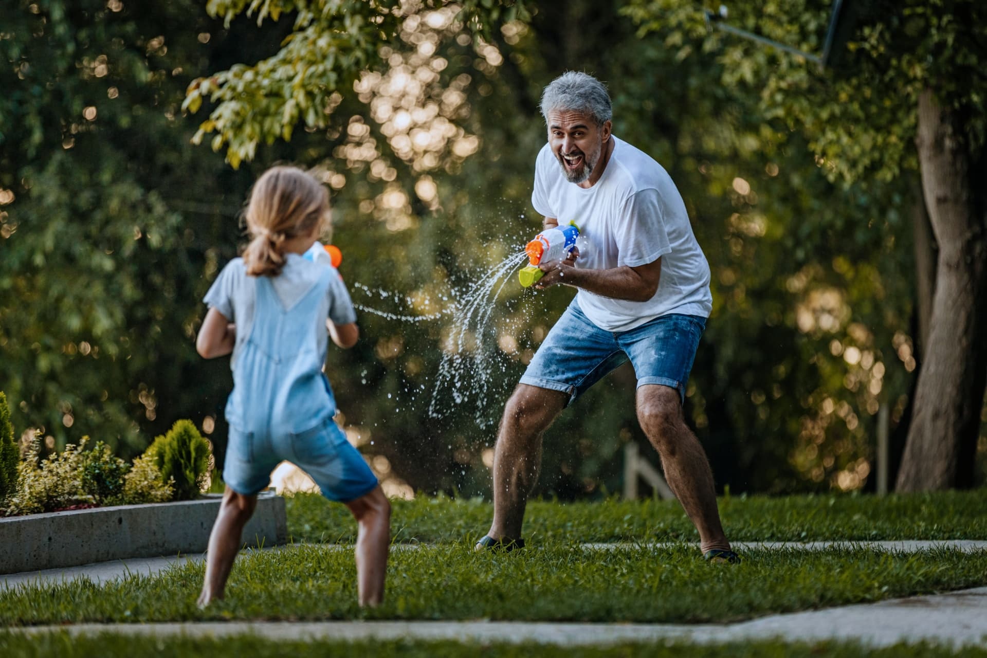 Friendly water gun fight in a garden between grandfather and his granddaughter.