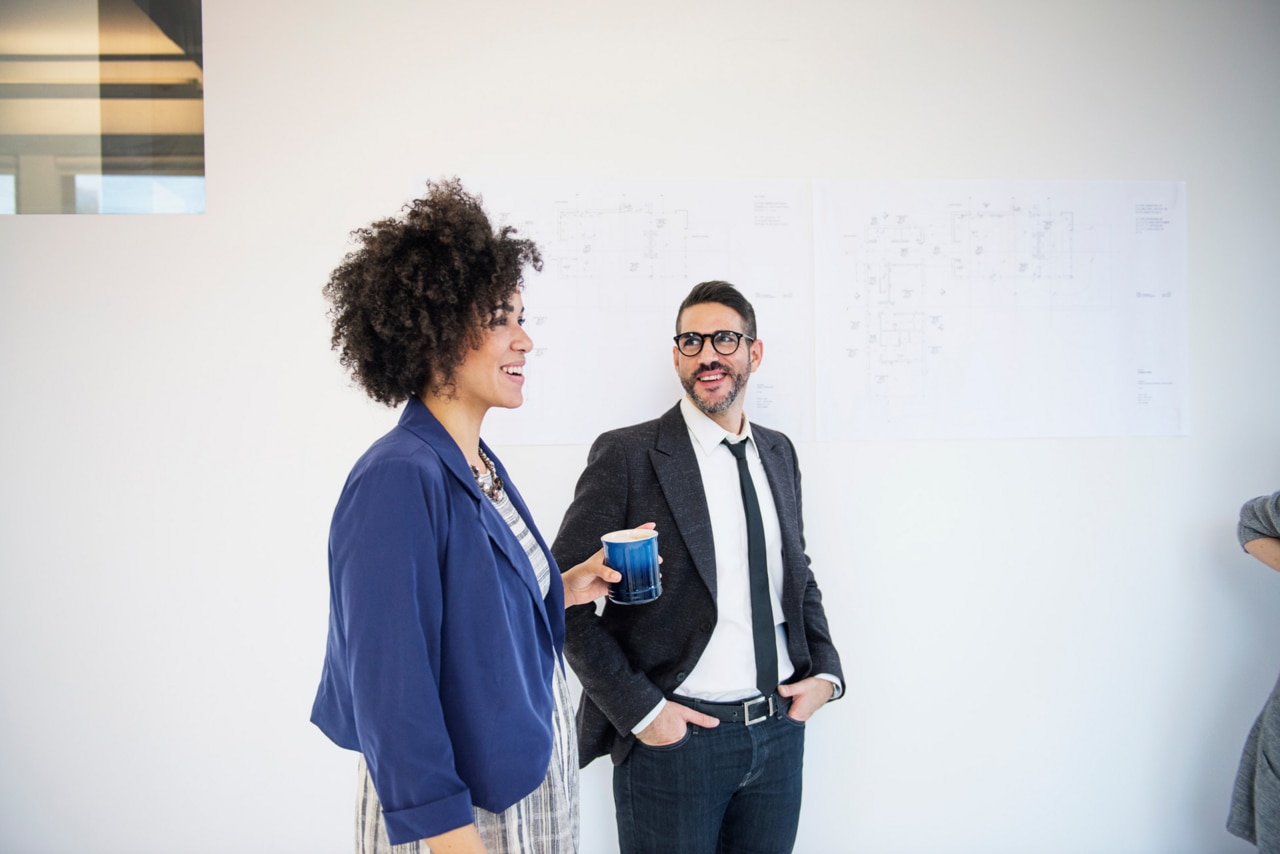 Two architects in their 30s standing in the office and smiling. Two architects in their 30s standing in the office and smiling.