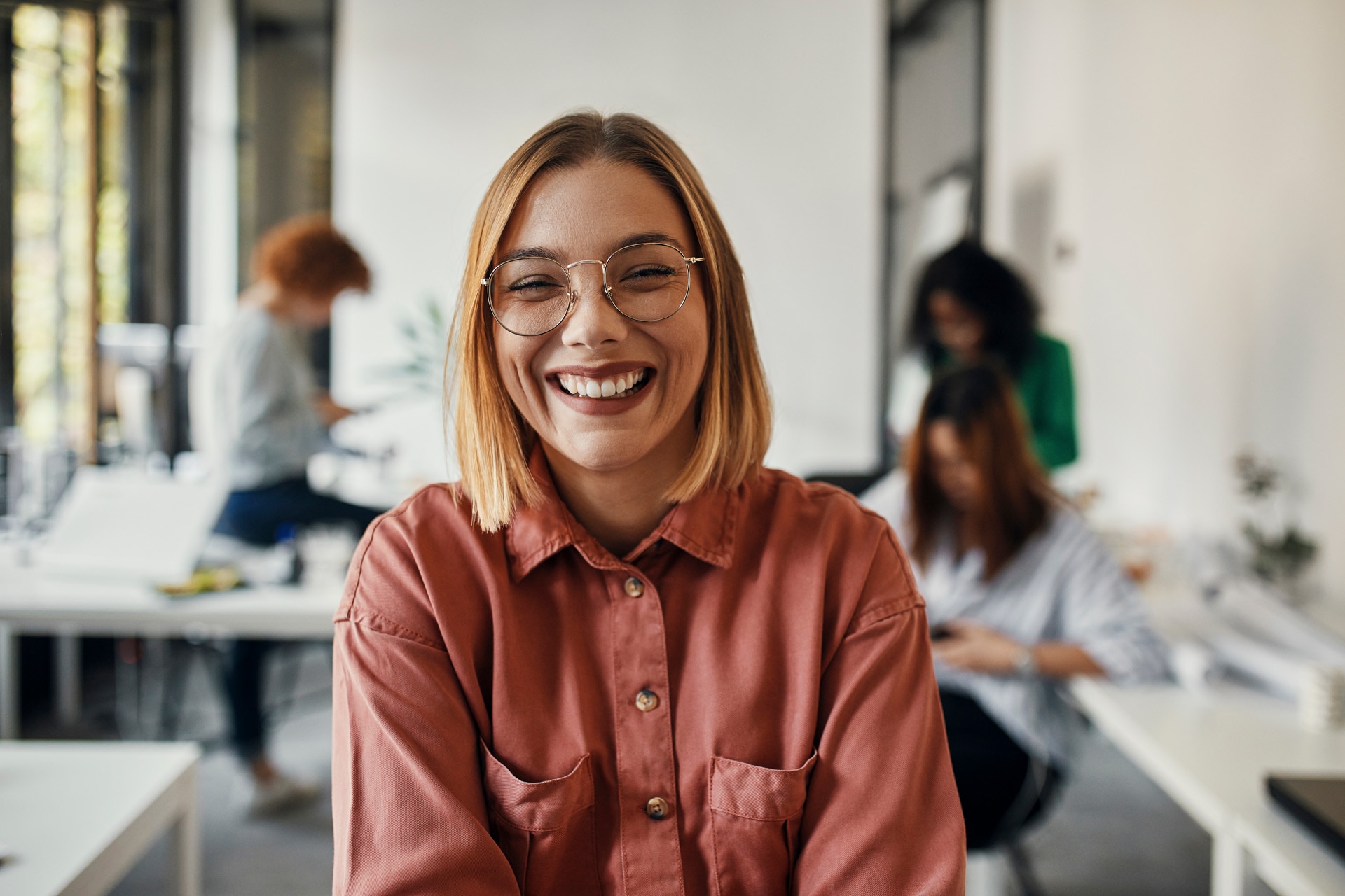 Portrait of a happy businesswoman in office with colleagues in background.