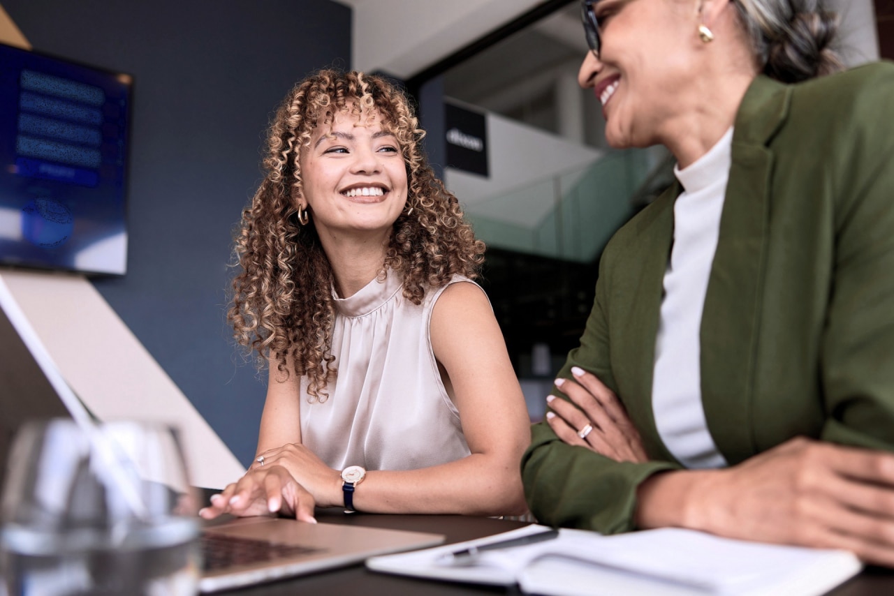 Two women smiling and working on a laptop